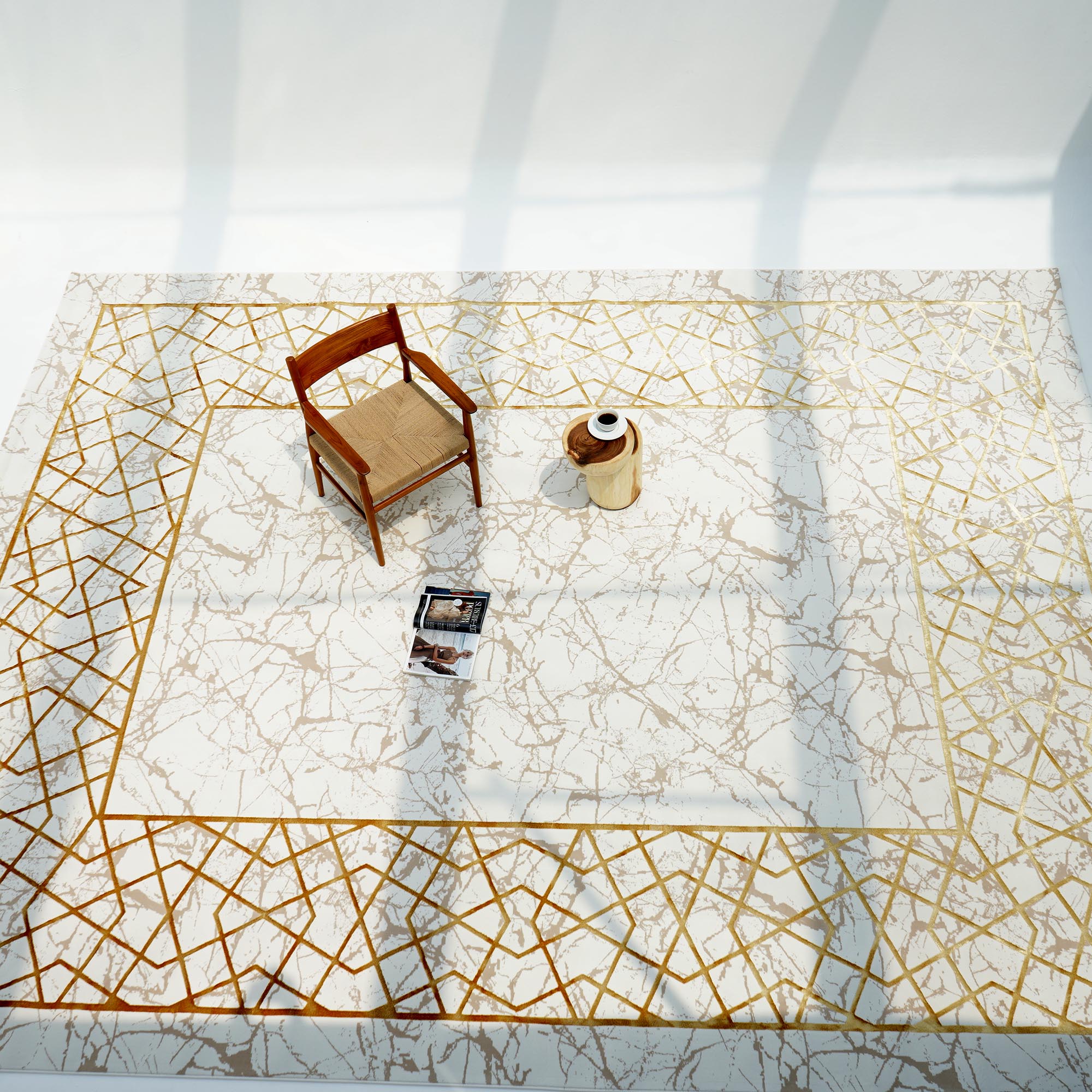 A wooden chair, ceramic vase, and open magazine sit on the RAMSHA HOME Cream Shrink Cream Colored Geometry Pattern Turkey Rug MZ67C, sunlight highlighting its gold lines and minimalist cream and ivory accents.