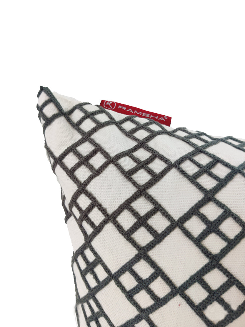 A close-up of the White And Grey Embroidery Cotton Cushion CS-262 by RAMSHA HOME, showcasing a white pillow with a black geometric grid pattern and a red RAMSHA tag at the corner, set against a plain white background.