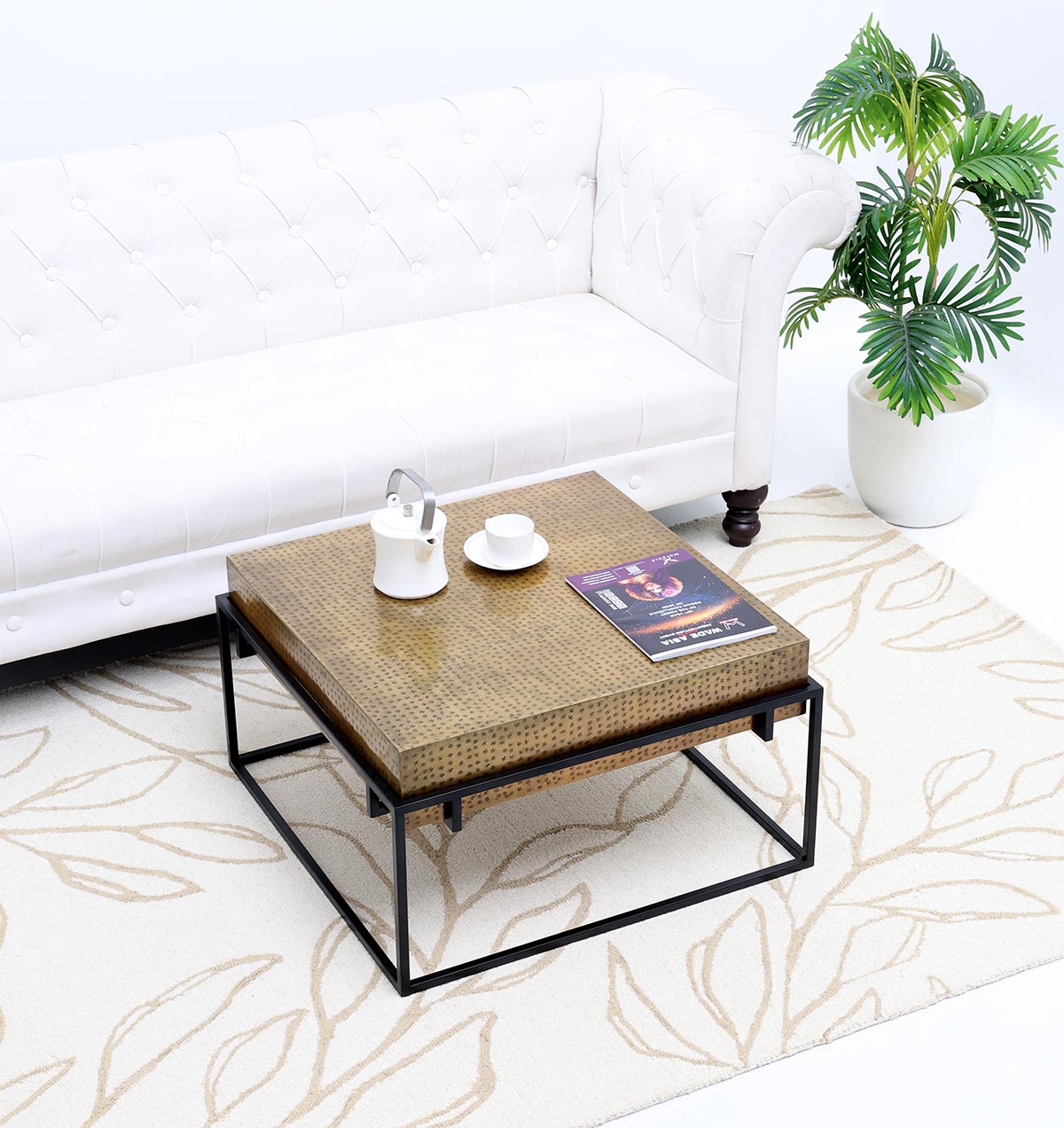 A modern living room with a white tufted sofa, the RAMSHA HOME Modern Round Coffee Table (solid wood top, black iron legs), a teapot and cup, magazine, beige patterned rug, and a potted plant in a white planter.