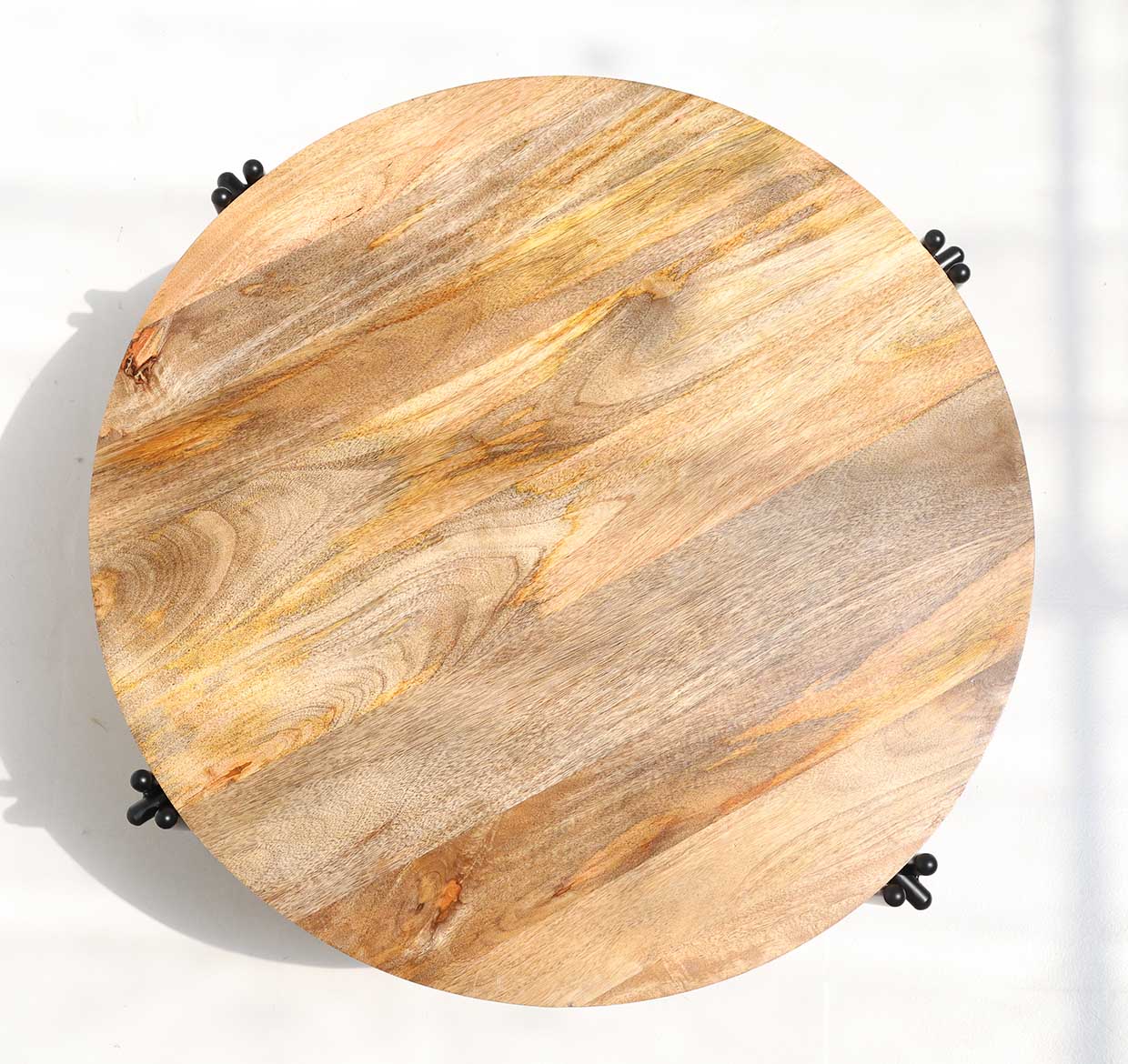 The RAMSHA HOME Modern Round Coffee Table (GH-067) features a solid wood top with natural grain and black iron legs, shown from above on a white surface with sunlight casting soft shadows across the table and background.