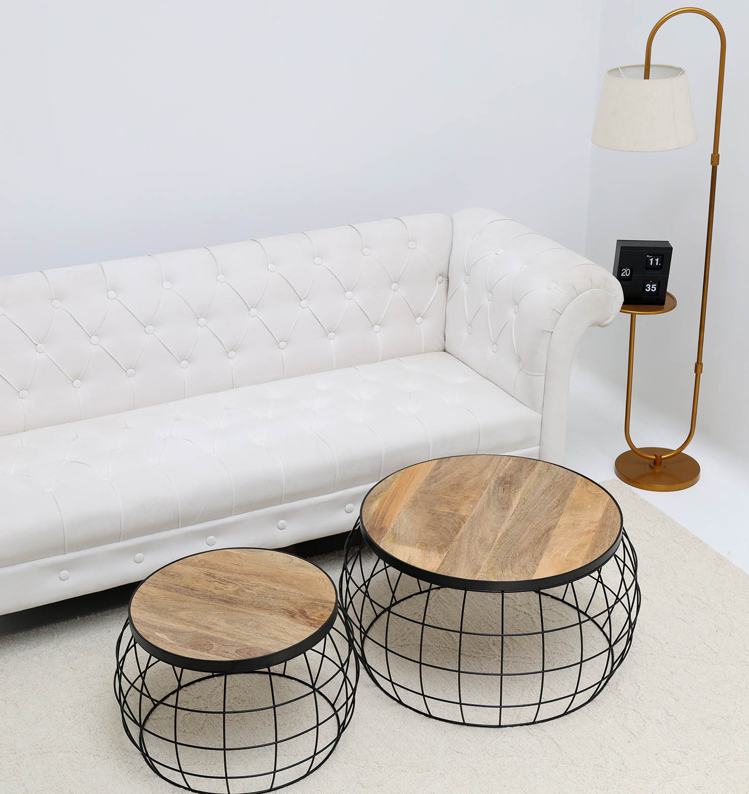 A modern living room featuring a white tufted sofa, two RAMSHA HOME Industrial Nesting Side Tables GH-068 with solid wood tops and metal wire bases, a standing lamp with a white shade, and a small side table holding a flip clock.