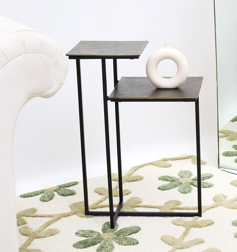 The RAMSHA HOME Modern Dual-Tier Side Tables (GH-075-A) feature antique brass tops and black iron bases, paired beside a white sofa on a patterned rug, with a circular-cutout white vase adding modern style.
