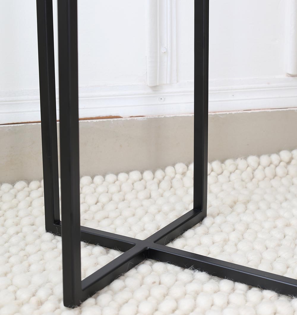 Close-up of the RAMSHA HOME Modern Dual-Tier Side Round Table (Copper Antique Finish, Black Iron Base GH-075-C), featuring black metal cross-shaped legs on a textured off-white chunky knit rug beside a beige wall with white trim.