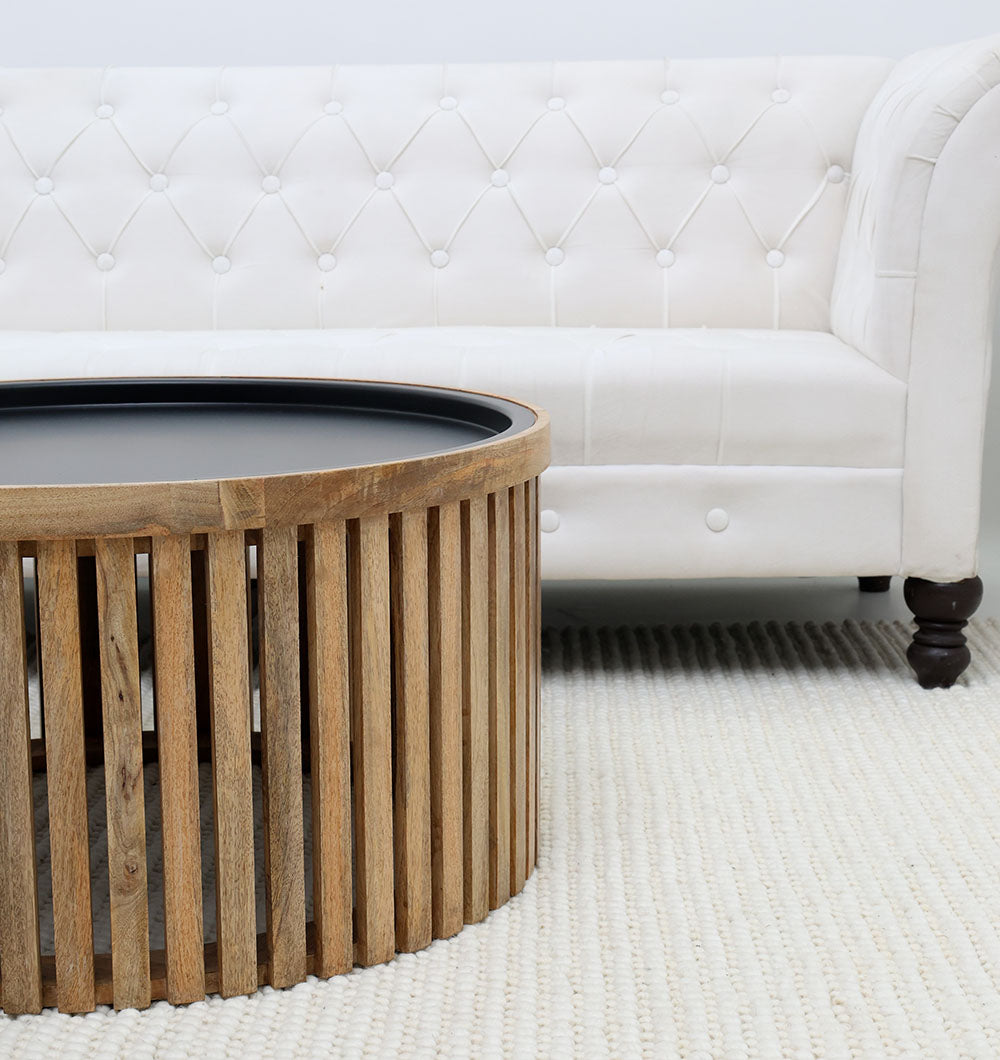 The RAMSHA HOME Modern Wooden & Iron Coffee Table (Round Slatted Design GH-093) sits on a textured cream rug in front of a white tufted sofa with dark wooden legs.