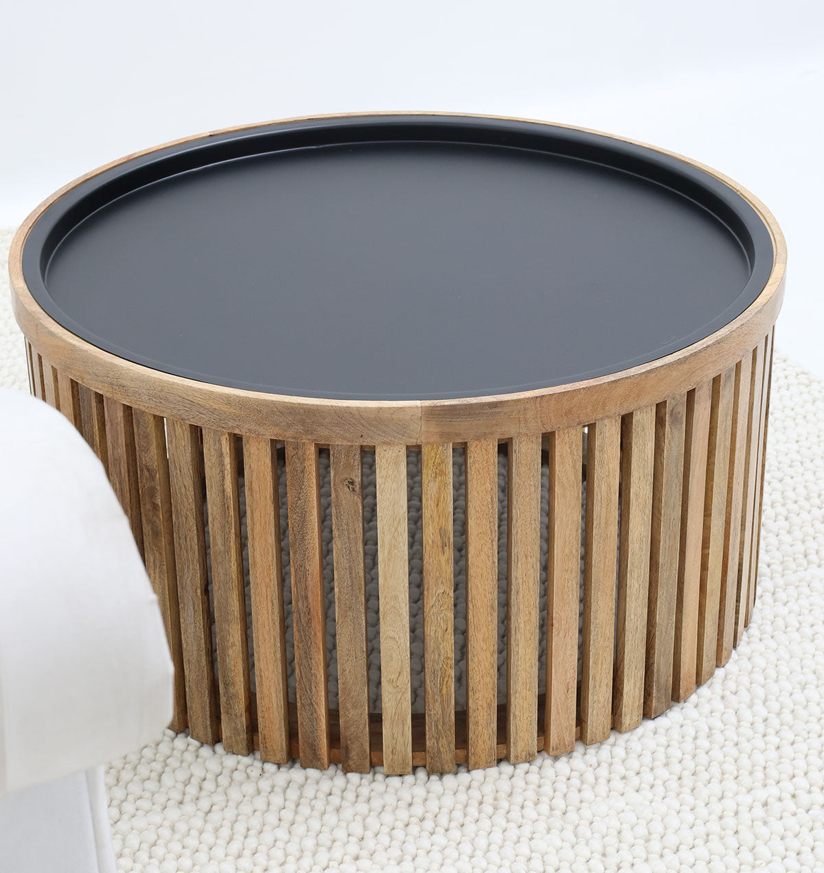 The RAMSHA HOME Modern Wooden & Iron Coffee Table (GH-093), featuring a round slatted base and flat black top, sits on a textured light rug beside a white sofa.