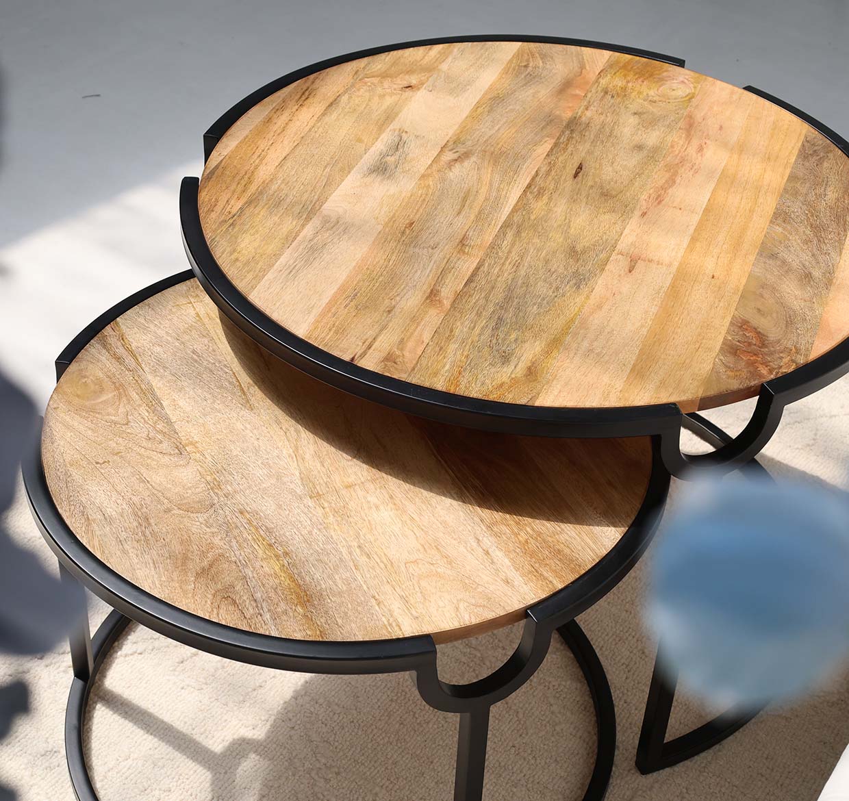 The RAMSHA HOME Modern Nesting Coffee Table Set (GH-094) features two round wooden-top tables with black metal frames, the smaller partially tucked under the larger, arranged on a light floor.