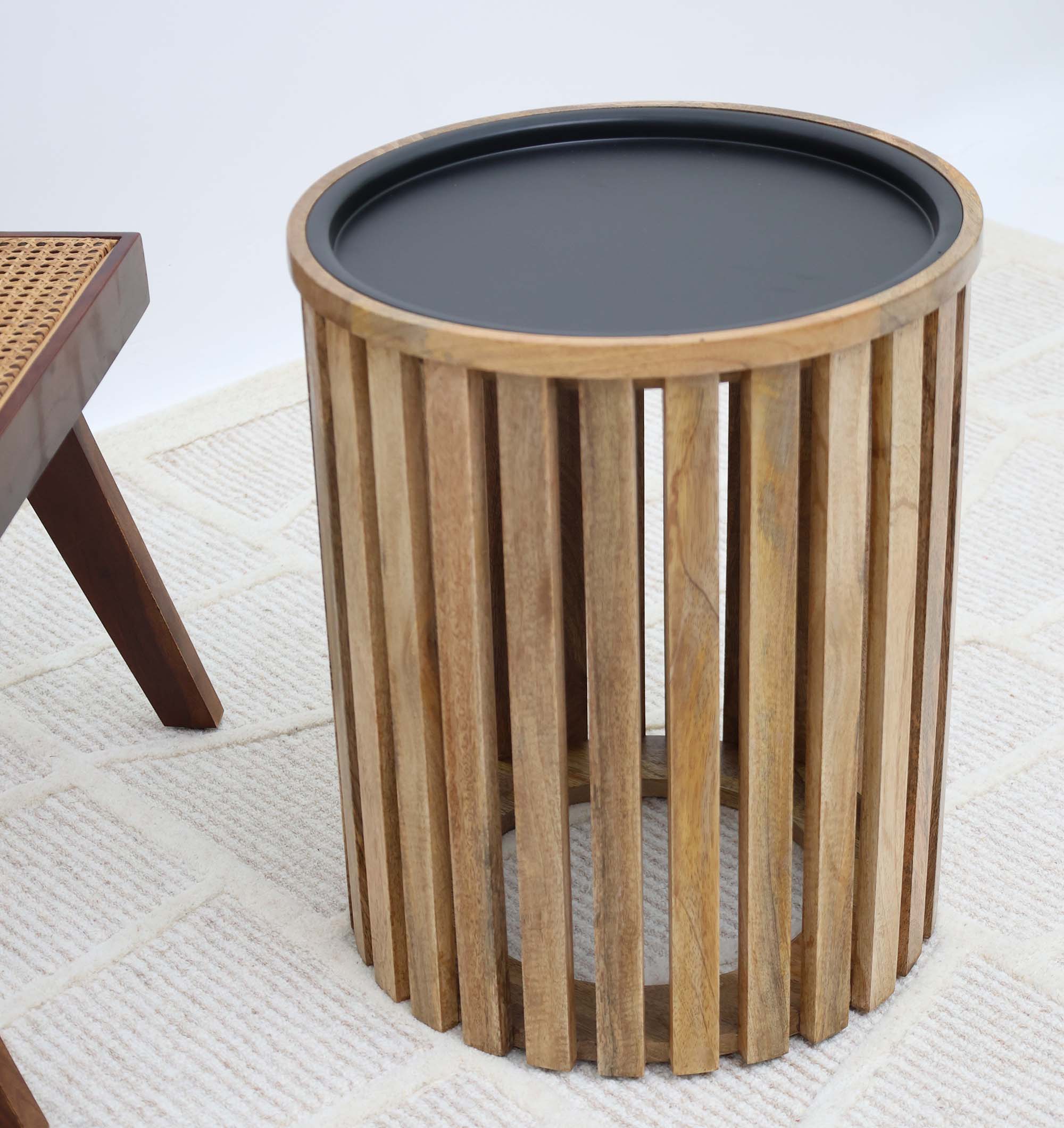 The RAMSHA HOME Modern Wooden & Iron Coffee Table – Cylindrical Slatted Design GH-097, featuring vertical slats and a black top, brings modern style to your space when placed on a light rug beside woven furniture.