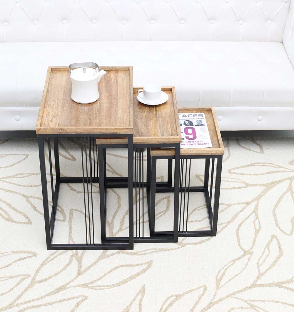In front of a white tufted sofa, two RAMSHA HOME Modern Three-Tier Side Tables (Natural/Black Powder Finish, Black Iron Base GH-099-A) display a teapot, cup on saucer, and newspaper atop a cream leaf-patterned rug.