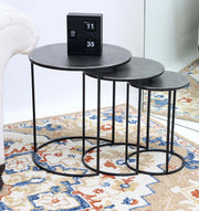 The RAMSHA HOME Set of 3 Modern Nesting Side Tables (Antique Brass Finish, Black Iron Base GH-071) are arranged by a white sofa on a patterned rug. A black flip clock adds modern style, with a mirror in the background.