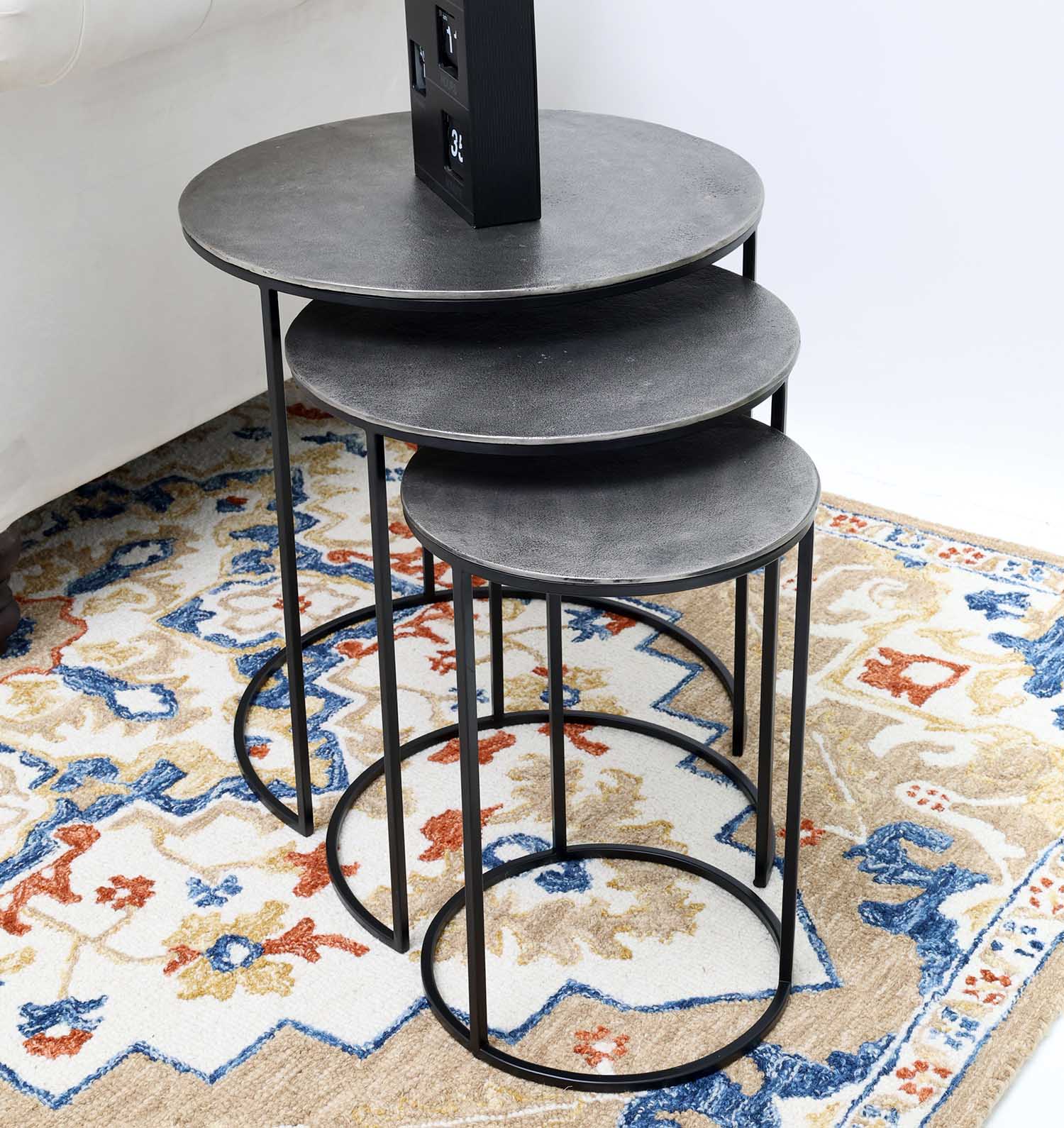 The RAMSHA HOME Set of 3 Modern Nesting Side Tables (Antique Brass Finish, Black Iron Base GH-071) adds modern style, stacked together on a blue, orange, and beige patterned rug beside a white sofa.