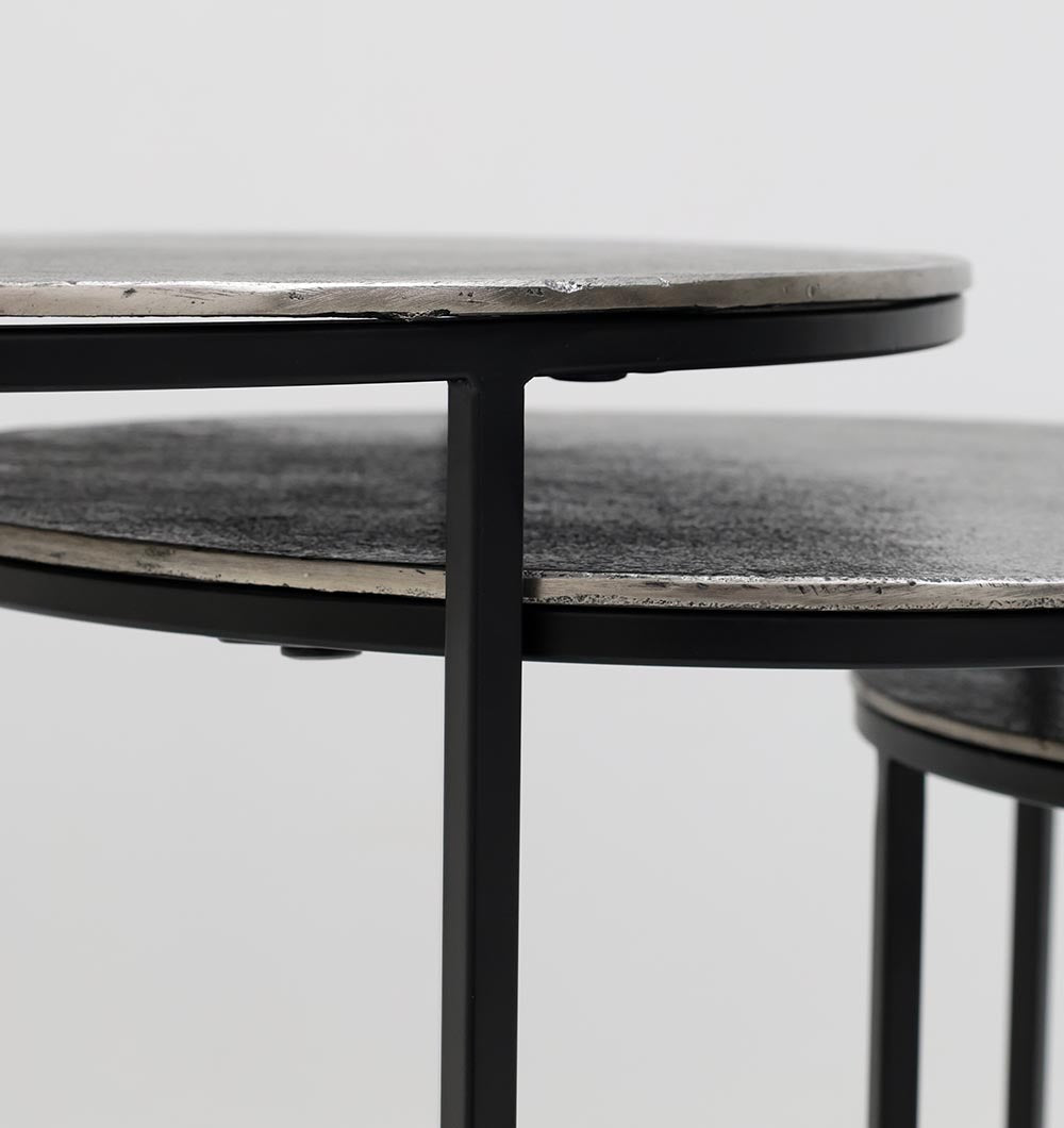 Close-up of RAMSHA HOME’s Set of 3 Modern Nesting Side Tables (GH-071), showing their antique brass tops and black iron bases with bold edges and legs, standing out against a plain background.