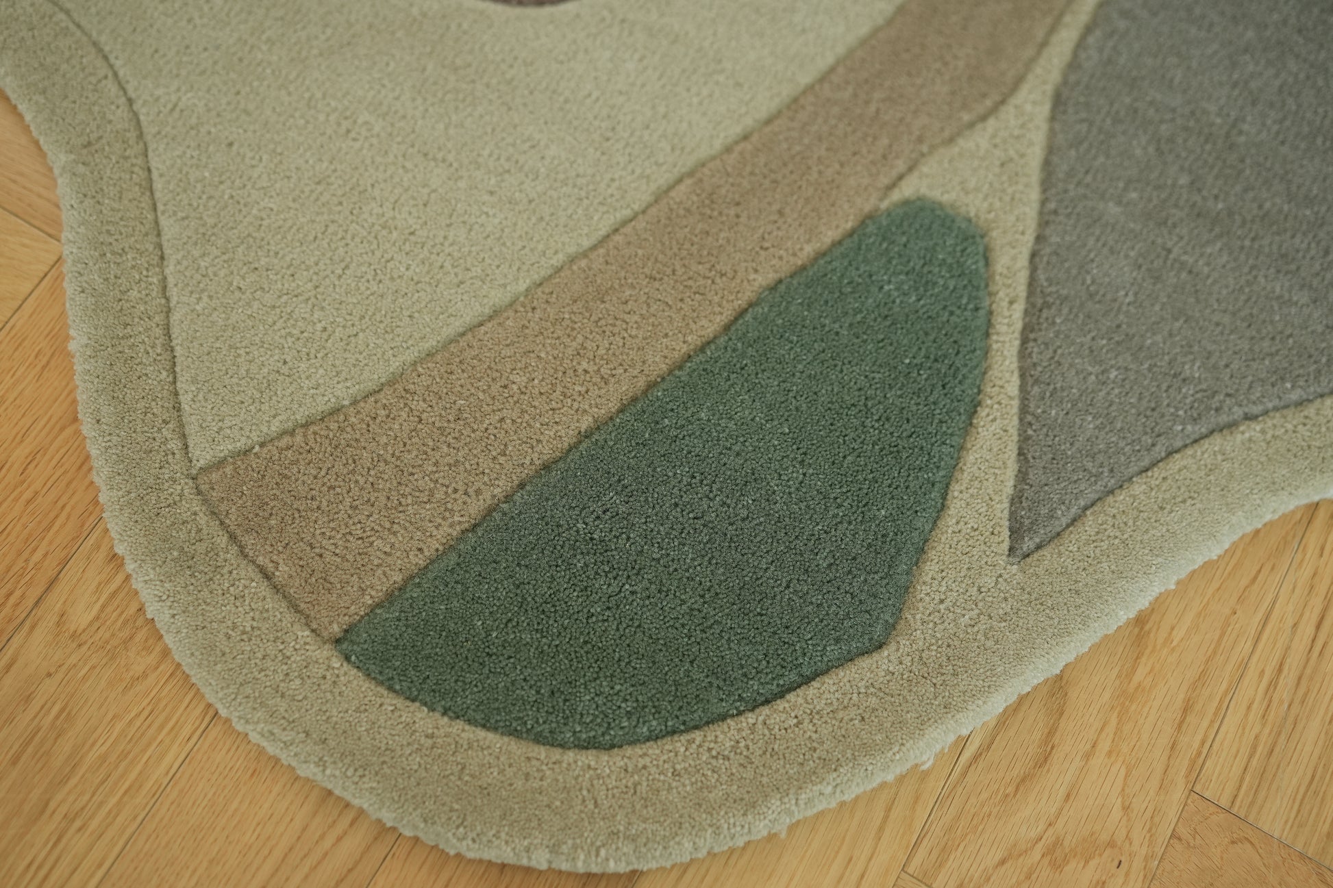 The RAMSHA HOME Handmade Multicolor Shaped Area Rug HTW 127 (200cm) features smooth curves, a soft texture, and organic shapes in beige, brown, green, and gray. Shown here on a light wooden floor for a modern abstract look.