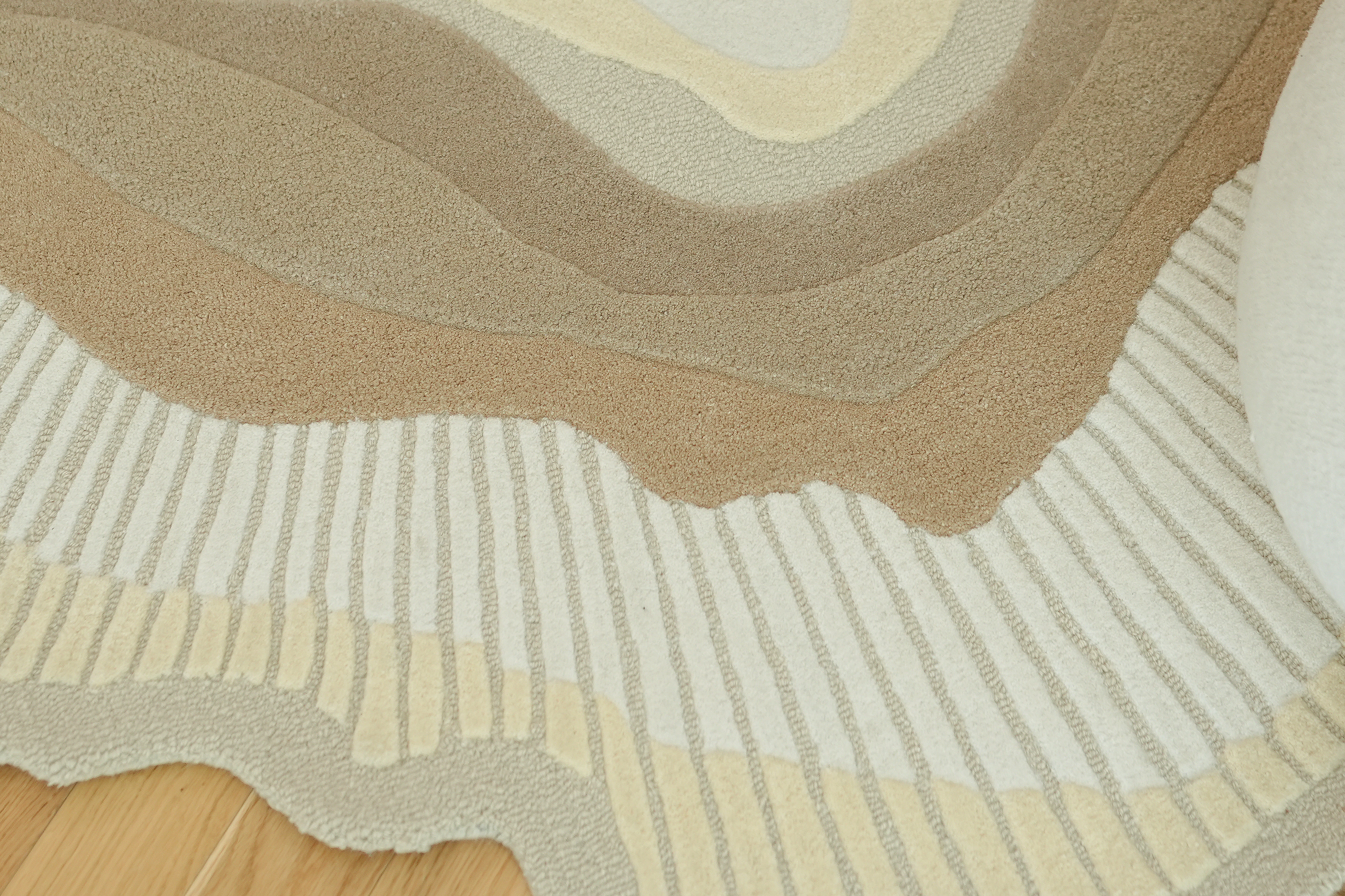 The RAMSHA HOME Handmade Shape Wool & Cotton Earth Tone Rug HTW 124 (200cm) features wavy, layered patterns in beige, tan, cream, and brown with textured lines and curves for a striking look on wooden floors.