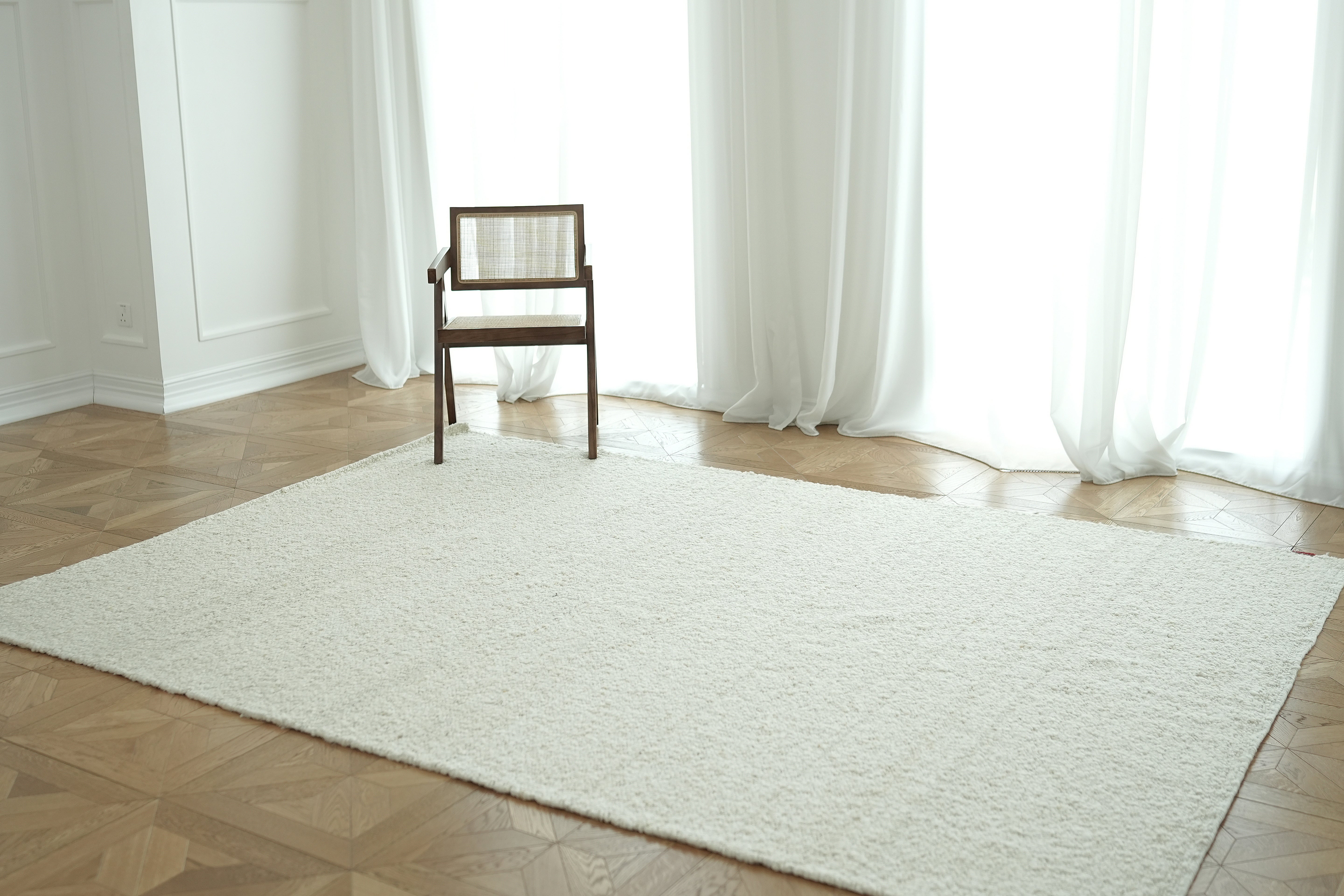 A wooden chair with a woven backrest sits on the RAMSHA HOME Handmade Natural Off White Woven Rug For Home Decor SR-059 in a bright room with wooden flooring and sheer white curtains.