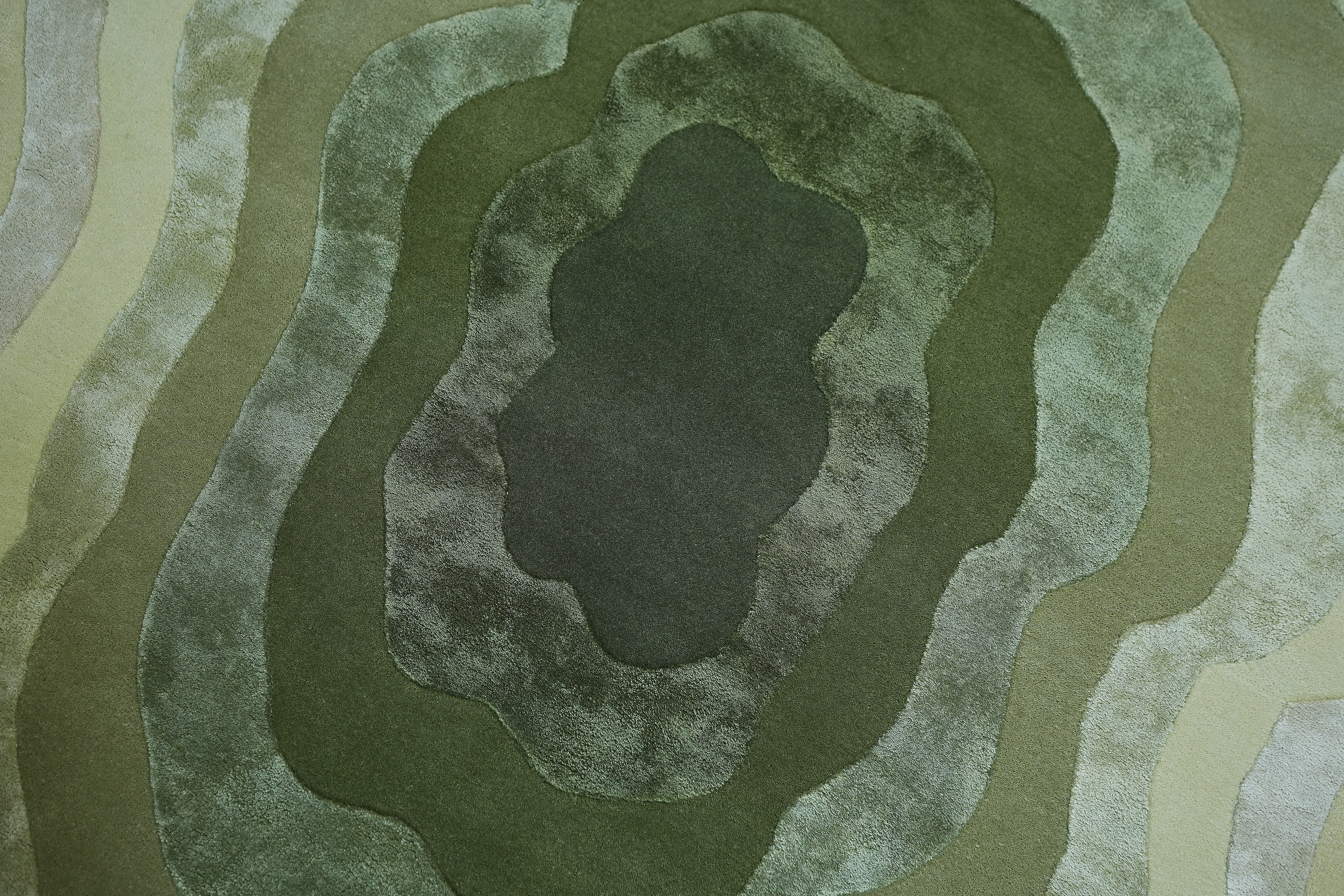 The RAMSHA HOME Handmade Shape Area Rug - HTWV 164 has a textured green surface with layered, irregular ovals resembling contour lines, hand-tufted in wool-viscose, transitioning from dark to light green.