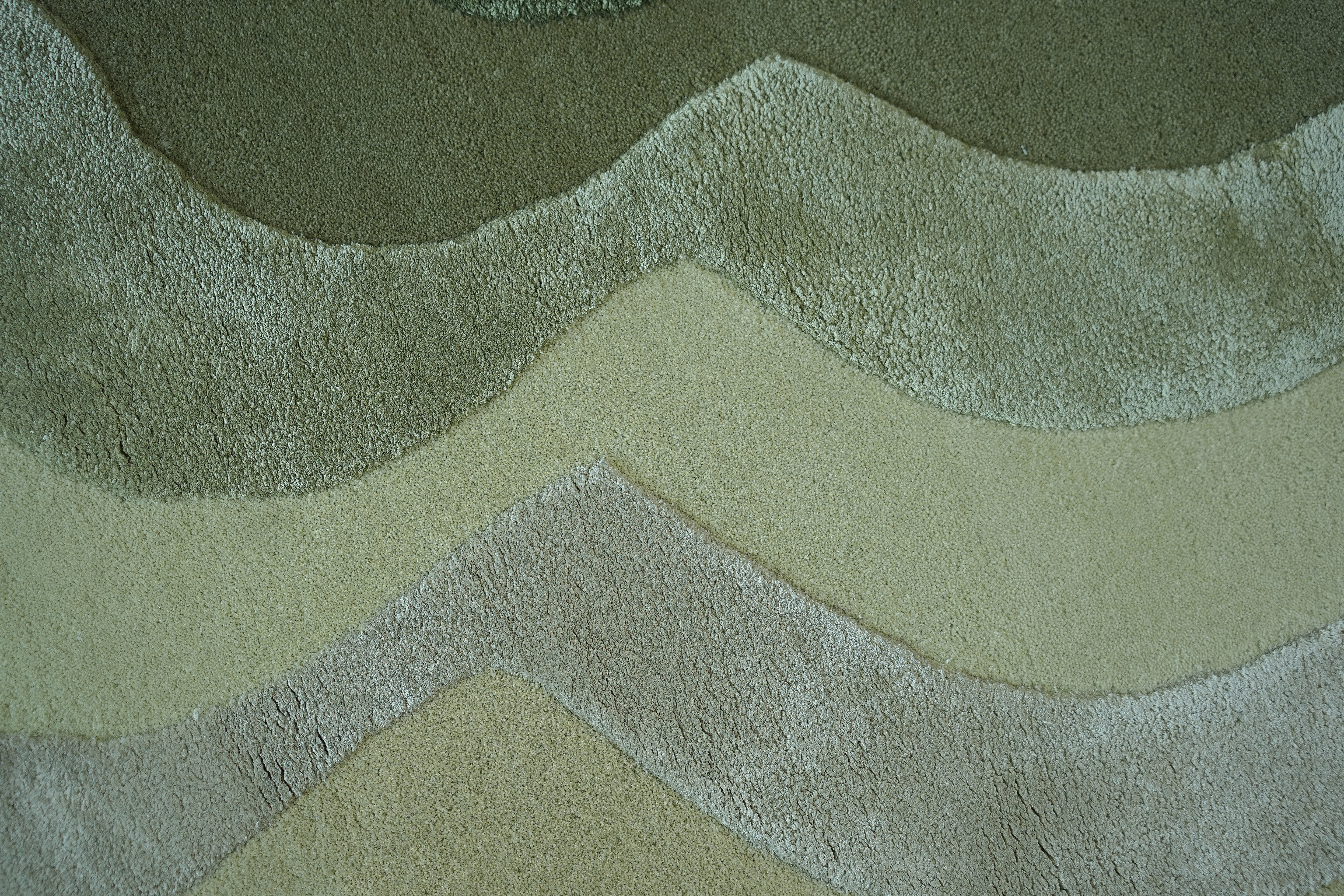 A close-up of the RAMSHA HOME Handmade Shape Area Rug - HTWV 164 showcases its soft, plush hand-tufted texture and wavy horizontal patterns in green, beige, and light gray tones.