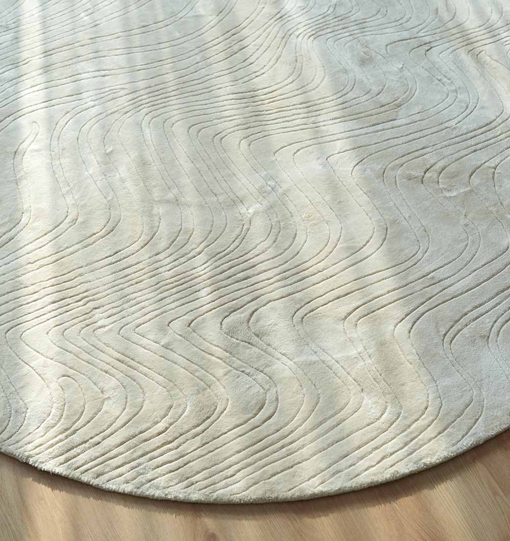 The Handmade Oval Shape Area Rug HL-04, in light beige with raised wavy patterns, is hand tufted and sits on a wooden floor bathed in soft natural light.