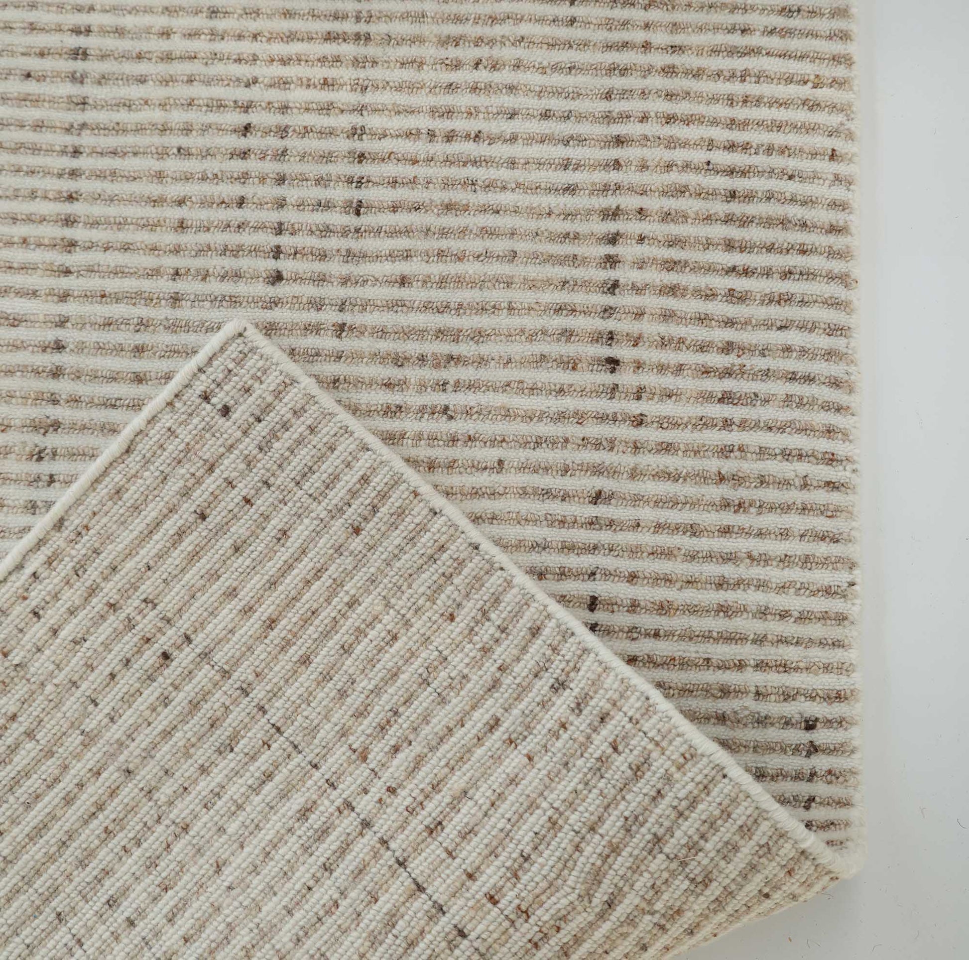Close-up of the RAMSHA HOME Handwoven Ivory Wool Rug Textured Area Rug (HLR-001), featuring thin, alternating light and dark cream stripes. One corner is folded to highlight its minimalist, neutral pattern on both sides.