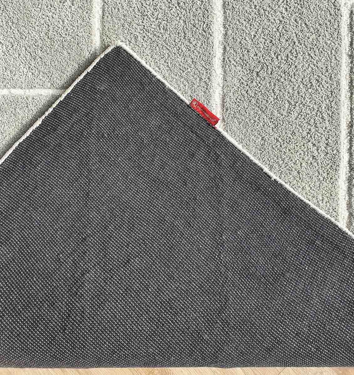 The Luxurious Handmade Rug - HTP 12 (300x400cm) by RAMSHA HOME is a textured grey geometric rug with a diamond pattern, featuring a dark gray non-slip backing and red tag, shown on a light wood floor with one corner flipped.