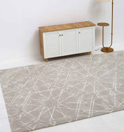 The RAMSHA HOME Decorative Rectangle Shape Rug HTP-15, light gray with a white geometric pattern, is placed on a white floor in front of a wooden cabinet with white slatted doors, beside a standing lamp with a round base.