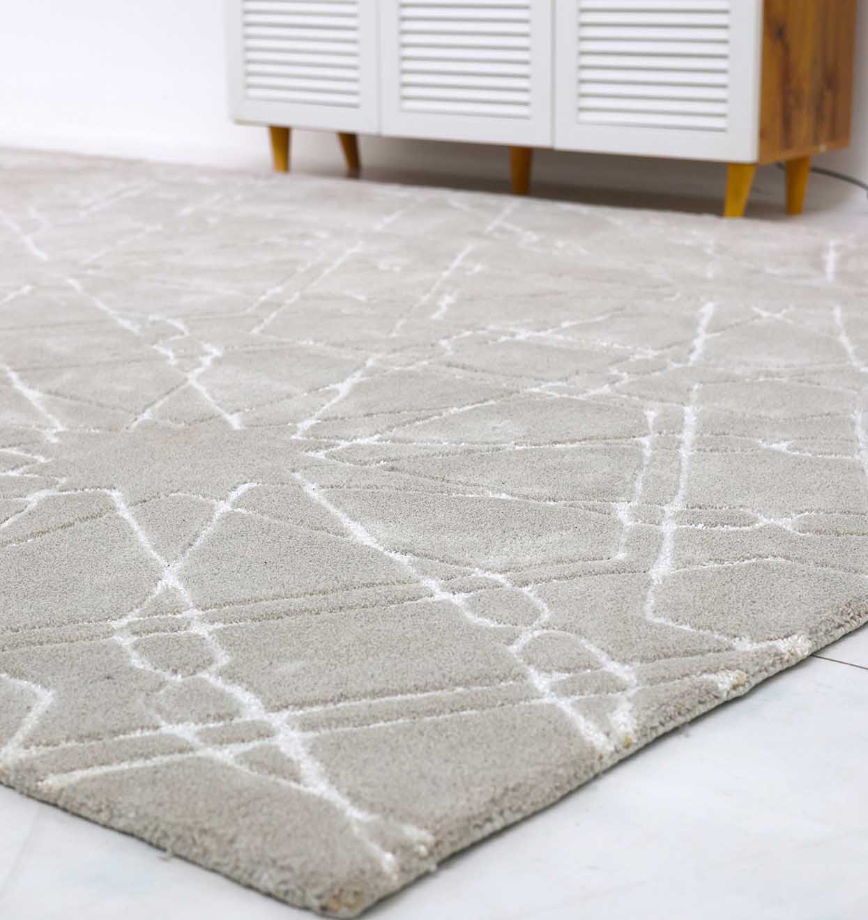 A close-up of the RAMSHA HOME Decorative Rectangle Shape Rug HTP-15, a hand-tufted geometric area rug in light gray with a subtle white pattern, placed on a white tiled floor before a white cabinet with wooden legs.