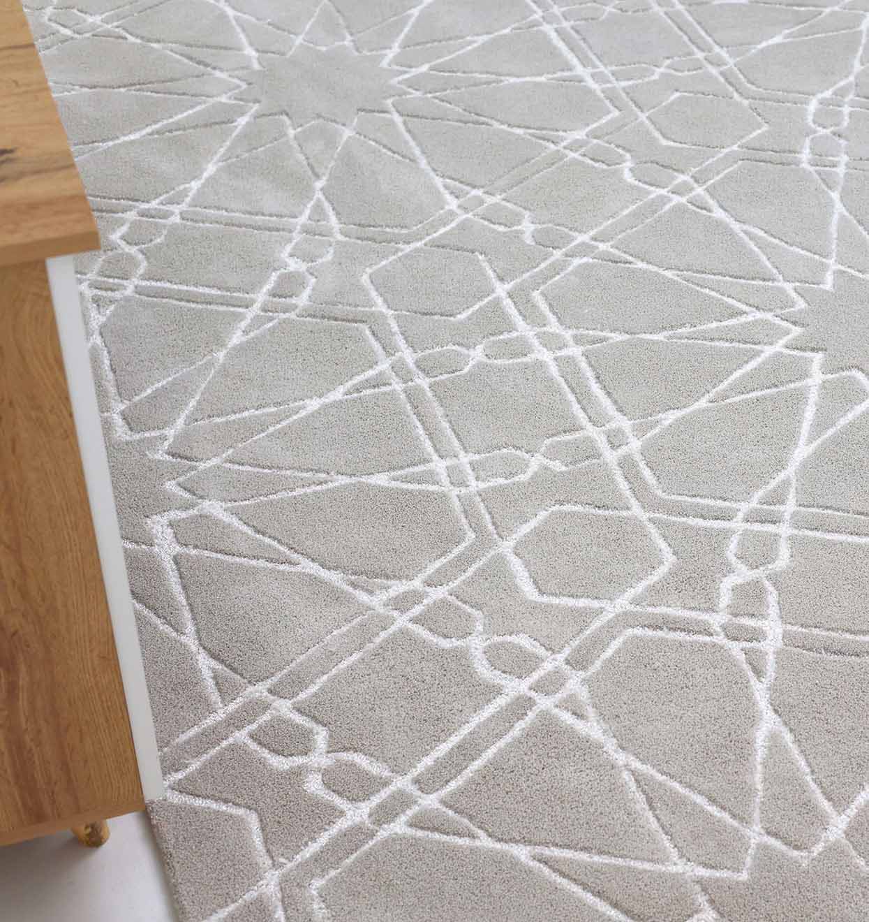 The RAMSHA HOME Decorative Rectangle Shape Rug HTP-15, featuring a light gray hand-tufted design with a raised white geometric pattern, is partially visible beside the edge of a wooden table.
