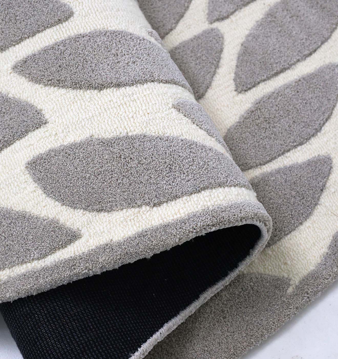 A close-up of the RAMSHA HOME Handmade Shape Rug HTP-16 in beige and gray shows its sculptural leaf pattern, textured surface, and black non-slip backing, partially rolled to highlight its modern design.