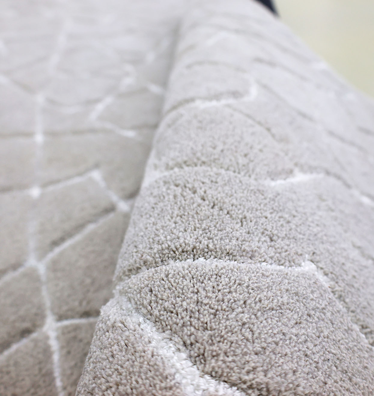 Close-up of the RAMSHA HOME Home Decor Area Rug HTP-17, a light grey hand-tufted rug featuring a geometric pattern, with its edge slightly lifted to showcase the plush surface and intricate transitional design.