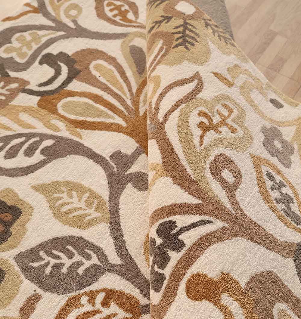 A close-up of the RAMSHA HOME Modern Polyester Handmade Carpet 170x240 Multi – HTP-24, showcasing its thickness and leaf design in beige, brown, and tan tones, partially folded back on a light wooden floor.