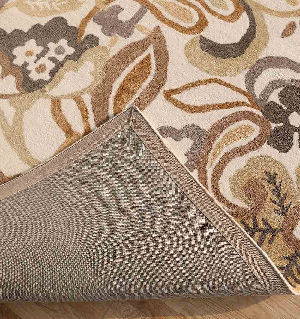 A close-up of the RAMSHA HOME Modern Polyester Handmade Carpet 170x240 Multi – HTP-24 shows its floral pattern in beige, brown, and cream. One corner is flipped to reveal the plain non-slip backing and edge stitching, resting on a wooden floor.