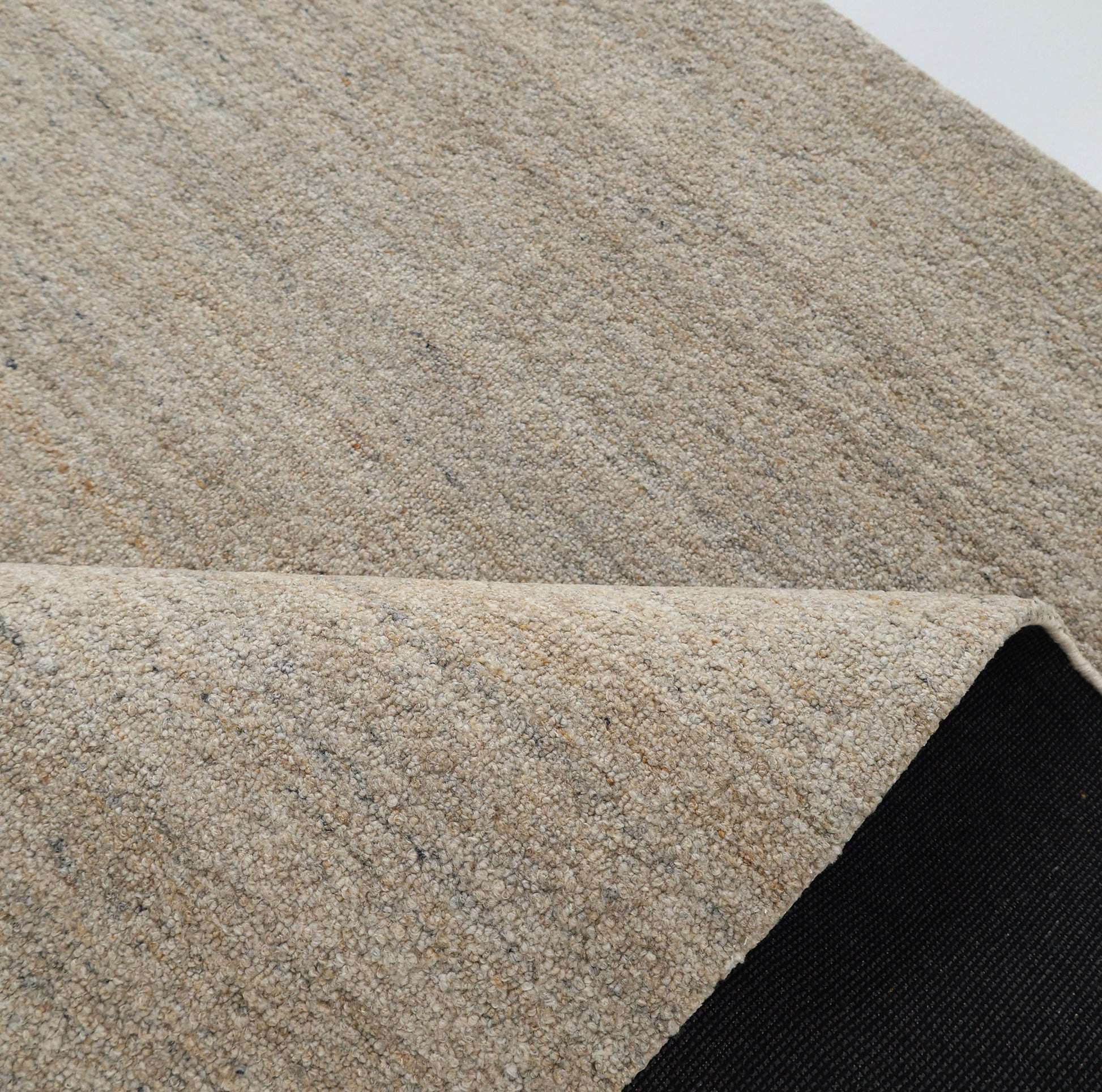 A close-up of the RAMSHA HOME Handmade Natural Wool Rug – Textured Beige Area Rug- HTP 25 shows its handwoven detail and folded corner, revealing a black non-slip backing beneath.