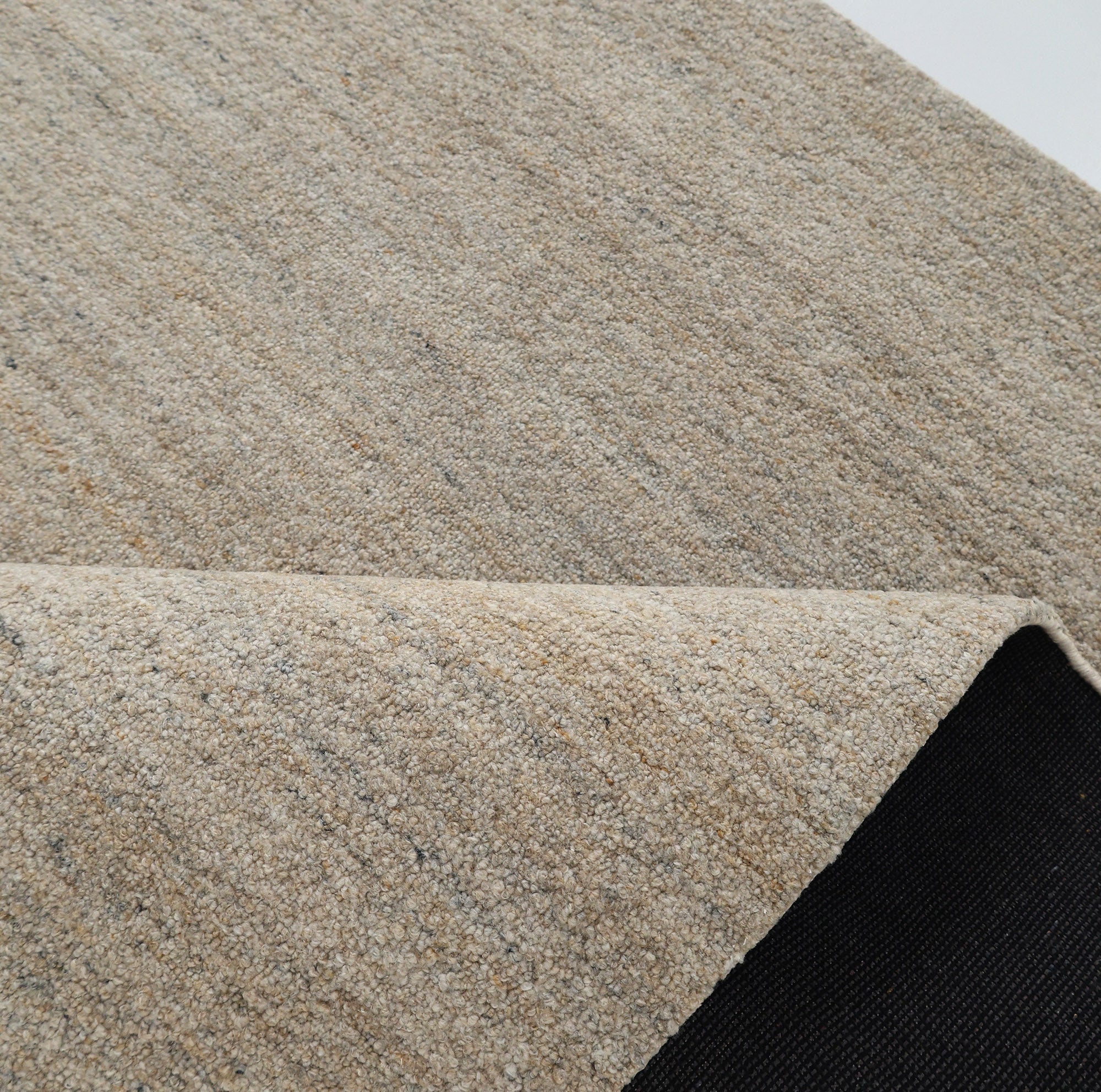 A close-up of the RAMSHA HOME Handmade Natural Wool Rug – Textured Beige Area Rug- HTP 25 shows its handwoven detail and folded corner, revealing a black non-slip backing beneath.