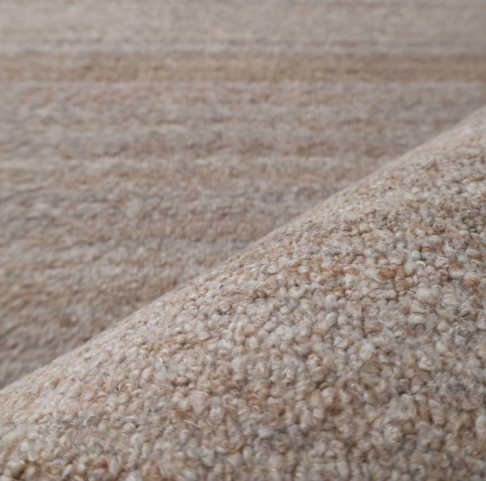 Close-up of RAMSHA HOME’s Handmade Natural Wool Rug – Textured Beige Area Rug- HTP 27, highlighting the looped beige fibers in the foreground; the softly blurred background reveals more of its minimalist textured surface.
