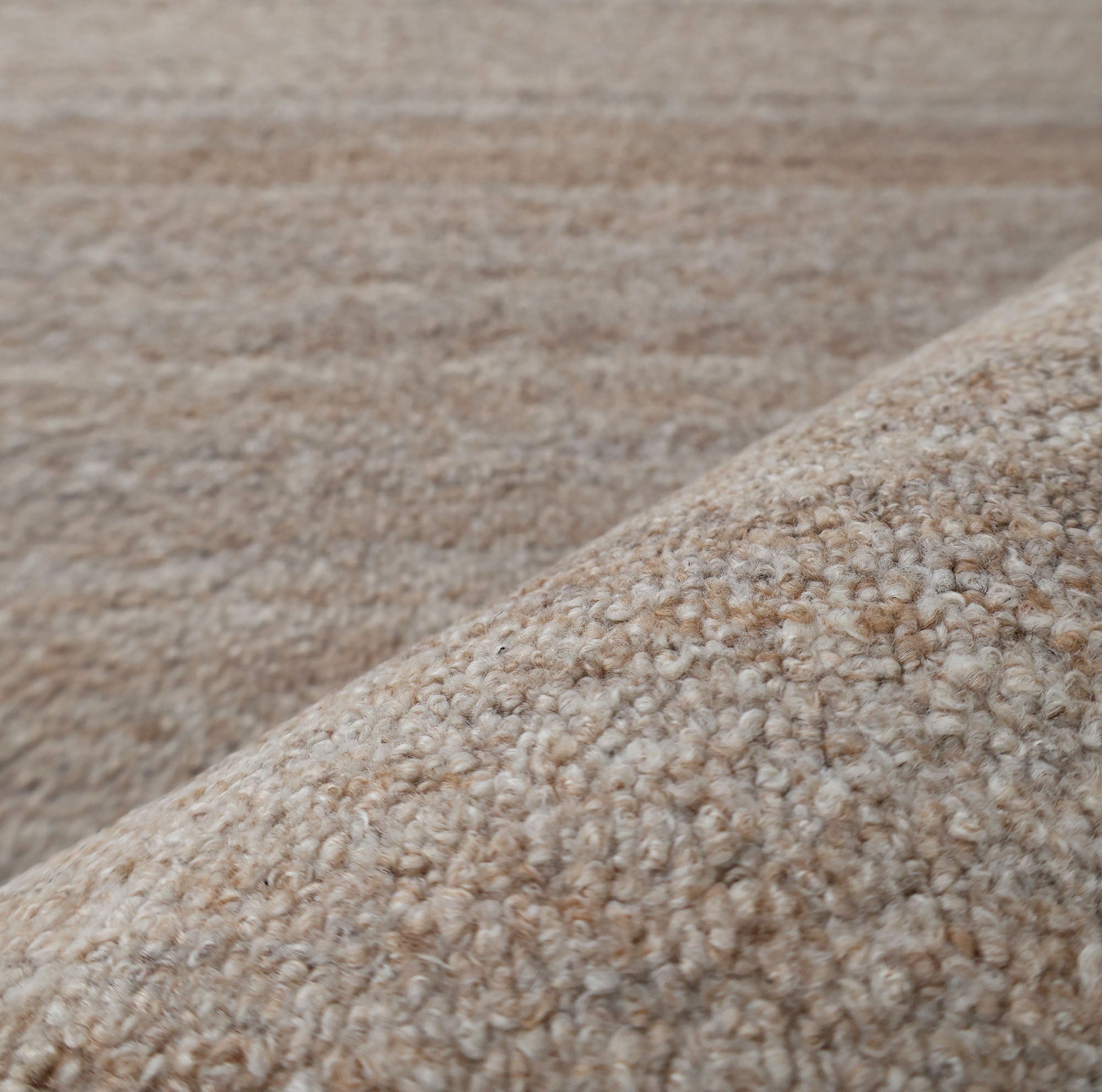 Close-up of RAMSHA HOME’s Handmade Natural Wool Rug – Textured Beige Area Rug- HTP 27, highlighting the looped beige fibers in the foreground; the softly blurred background reveals more of its minimalist textured surface.