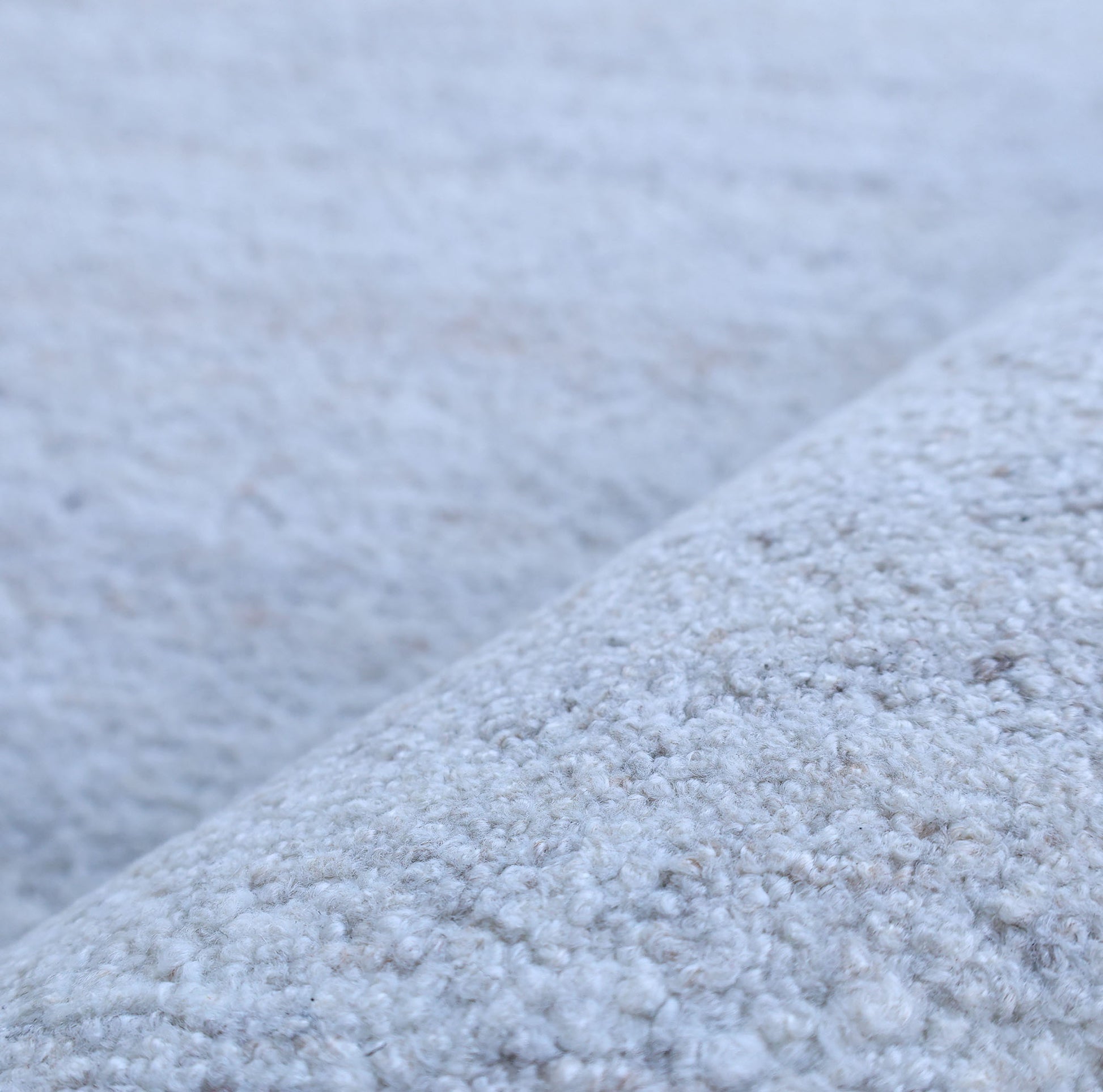 Close-up of the Natural Ivory Handmade Wool Rug – Modern Luxury Area Rug HTP 28 by RAMSHA HOME, showing its minimalist design, light gray textured surface, soft looped wool fibers, and a gentle fabric fold.