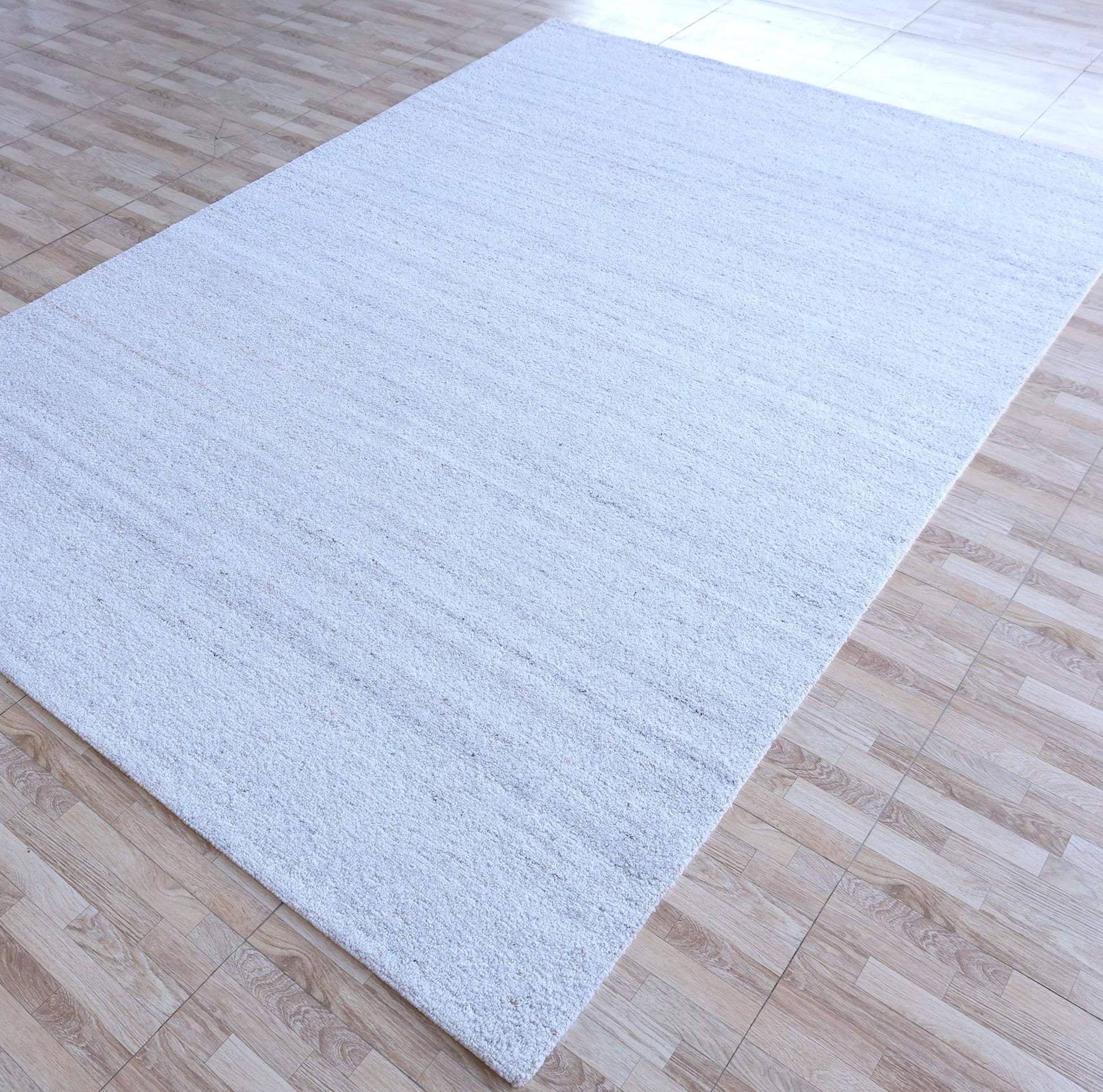 The RAMSHA HOME Natural Ivory Handmade Wool Rug – Modern Luxury Area Rug HTP 28, featuring a minimalist textured design, is laid over beige and light brown square tiles, covering much of the floor.