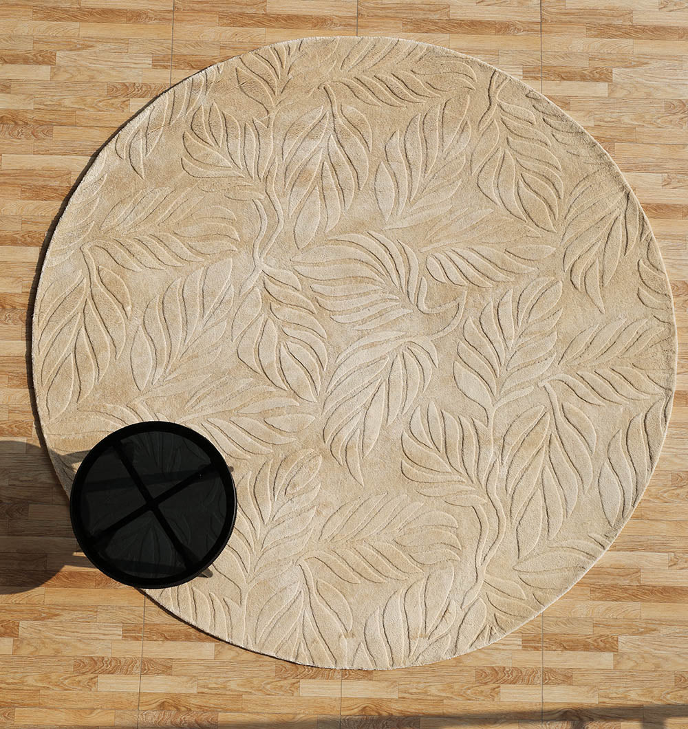 The RAMSHA HOME Beige Color Indoor Handmade Area Rug - HTV 15 with a raised leaf pattern sits on a wooden floor, partially supporting a small round black table on its edge.