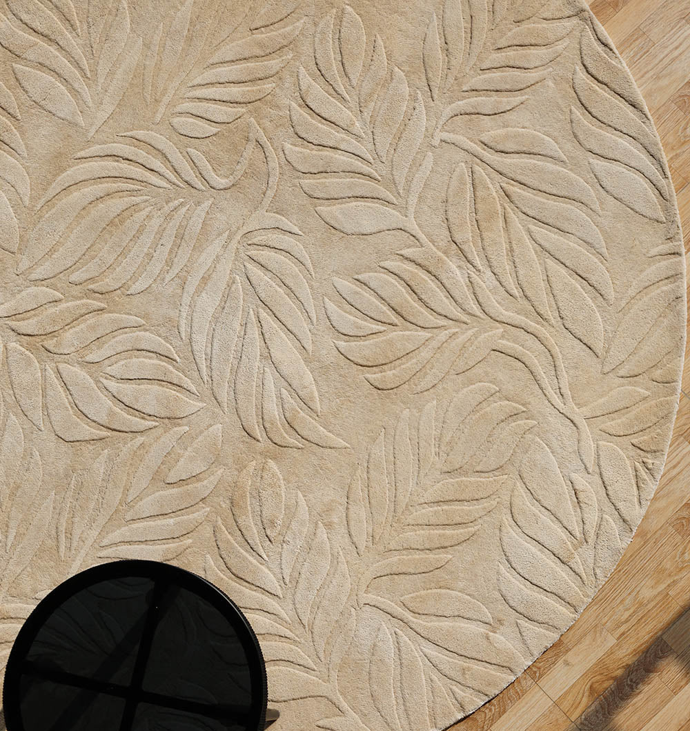 The Beige Color Indoor Handmade Area Rug - HTV 15 by RAMSHA HOME, featuring a raised leaf pattern, lies on a wooden floor. A small round black table is partially visible in the lower left corner.