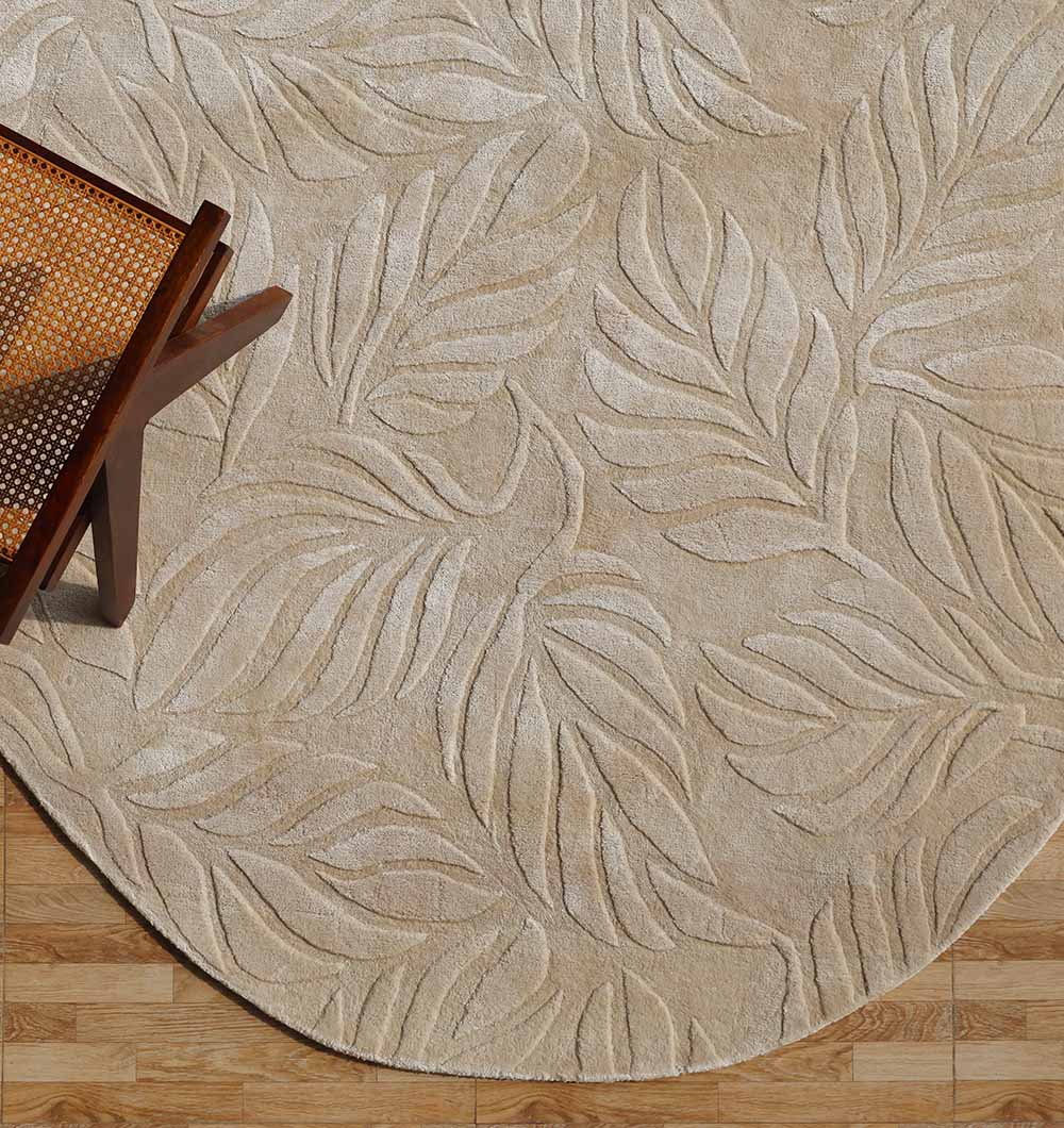 The RAMSHA HOME Beige Color Indoor Handmade Area Rug - HTV 15, featuring a subtle leaf pattern, is placed on a wooden floor. The edge of a mid-century modern wooden chair with a woven seat appears in the upper left corner.
