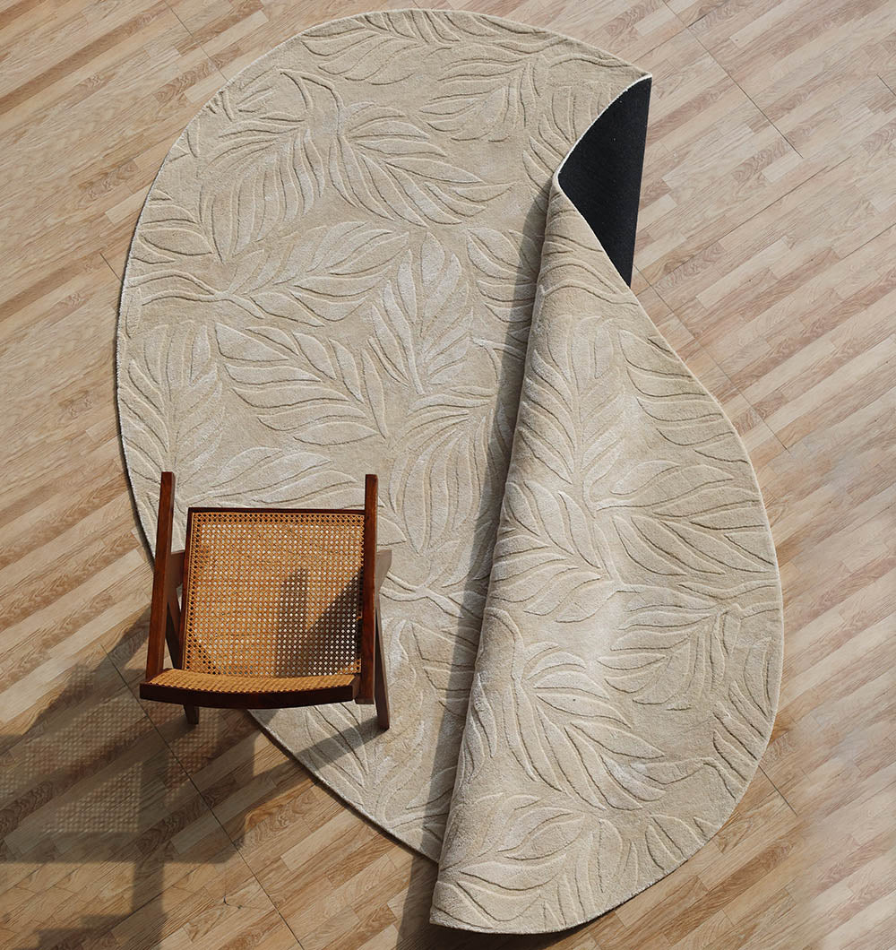 The RAMSHA HOME Beige Color Indoor Handmade Area Rug - HTV 15, featuring a delicate leaf pattern, is partially folded on a light wood floor with a wooden chair with woven seat partly resting on the rug and the floor.
