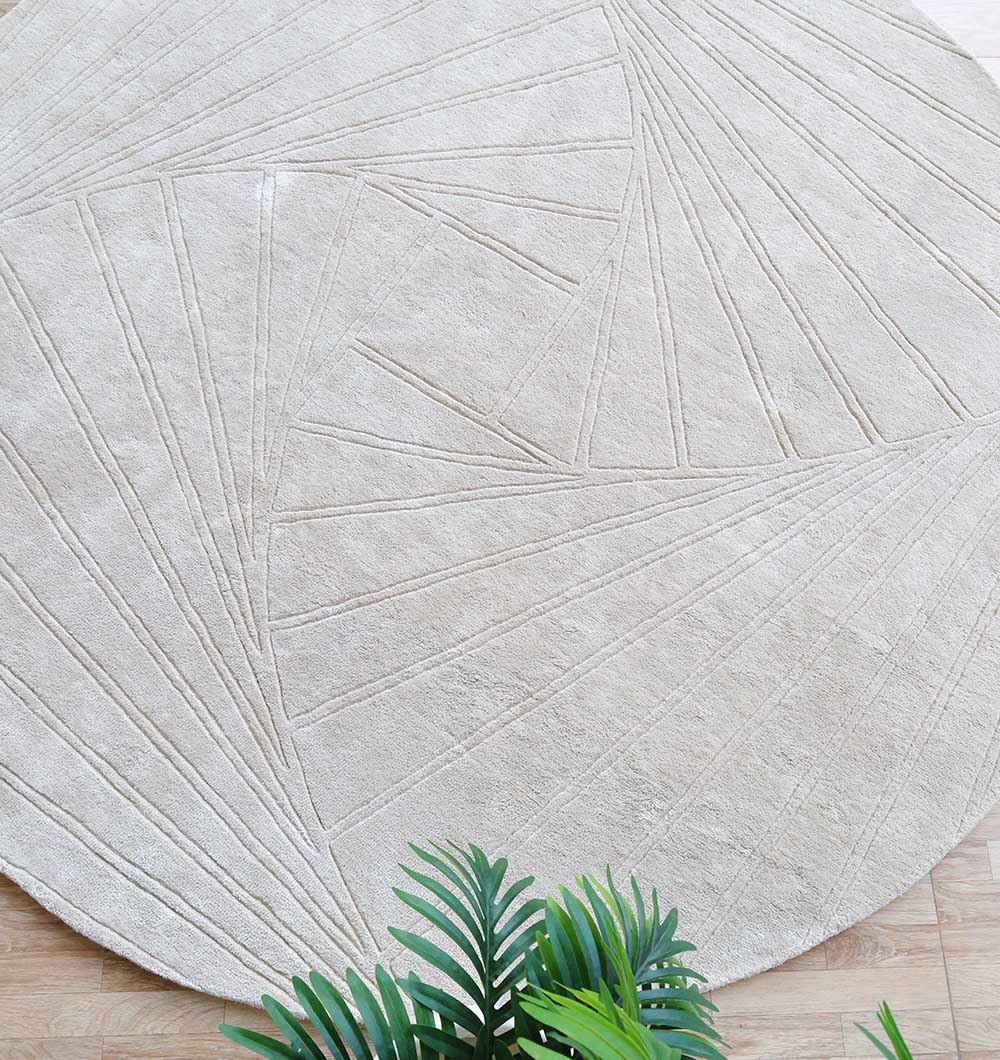 The RAMSHA HOME Handmade Rug - HTV 16 (200cm), a large neutral round rug with geometric linear patterns, sits on a light wooden floor. Green plant leaves are visible in the image corner.