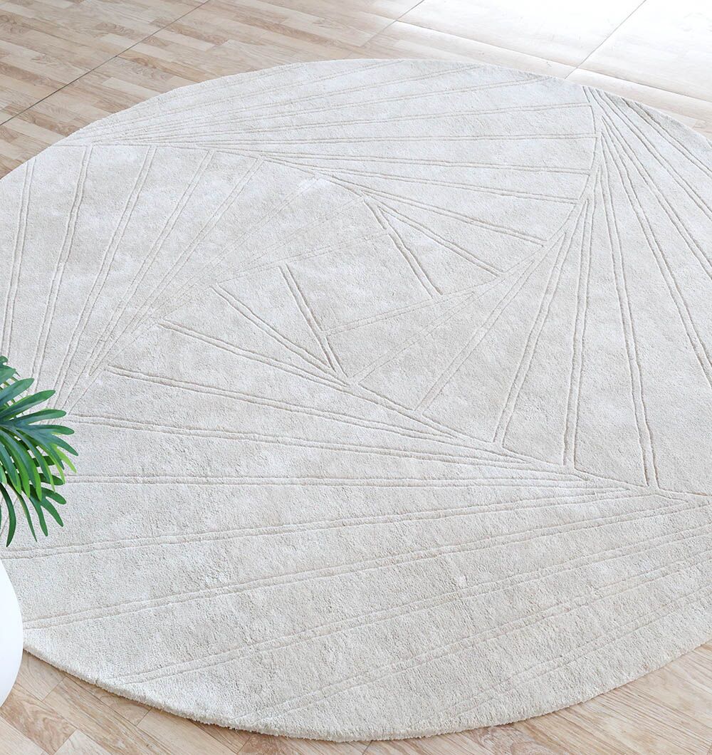 The RAMSHA HOME Decor Handmade Rug - HTV 16 (200cm), a neutral round wool rug with subtle geometric lines, adds warmth and texture to a light wood floor. A green plant in a white pot is partially visible in the lower left corner.