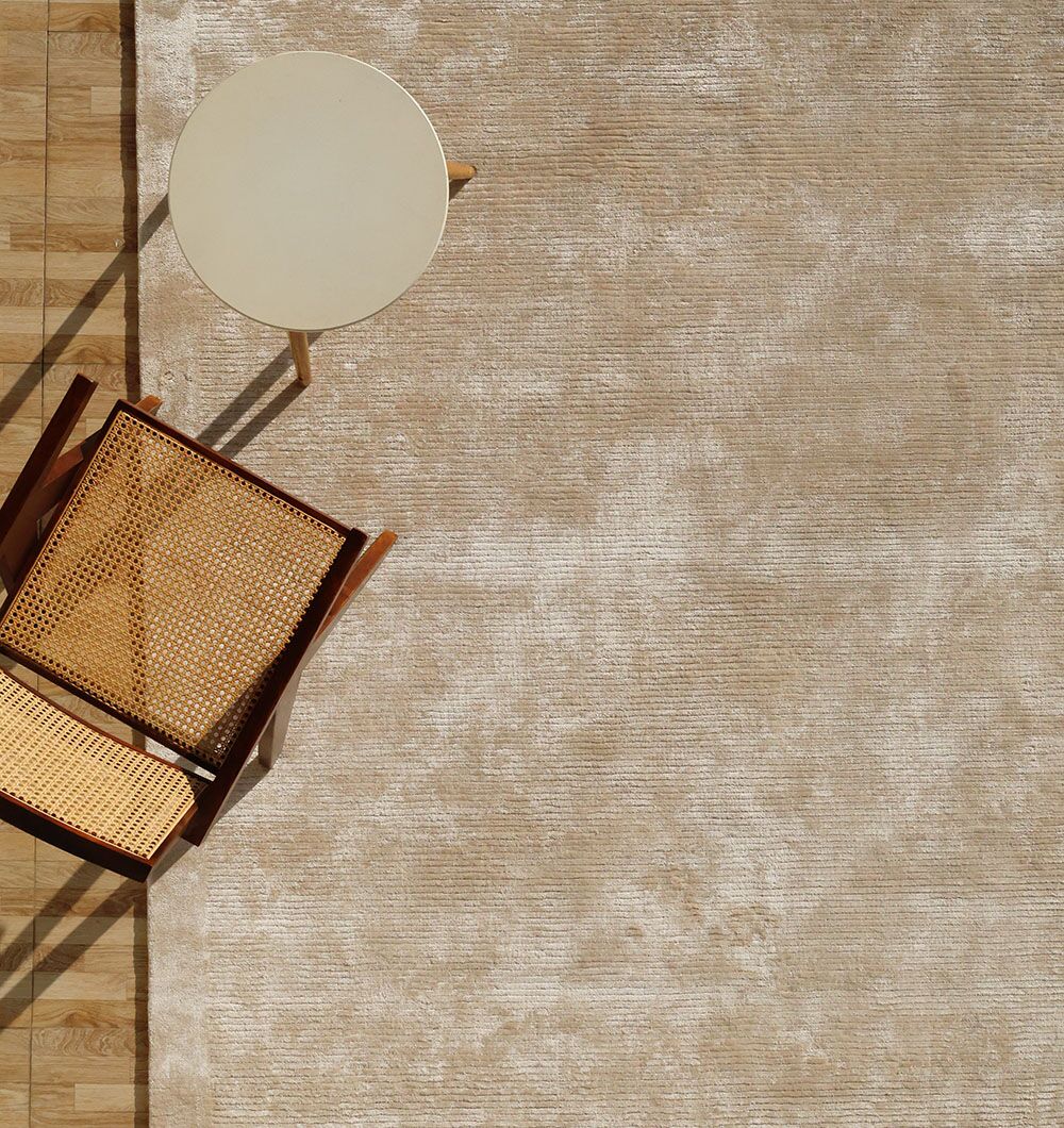 A top-down view of a wooden chair with a woven seat and backrest beside a small round beige table, placed on the RAMSHA HOME Beige Color Handmade Rug - HTV 18 (200X300 cm) over a wooden floor.