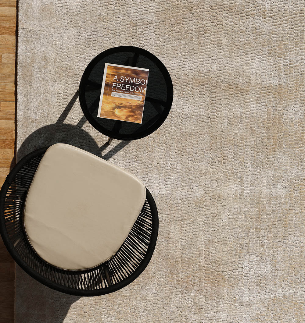 A black round chair with a beige cushion sits next to a small black side table holding “A Symbol of Freedom,” all placed on the RAMSHA HOME Beige Color Handmade Area Rug - HTV 20 (300X400 cm) with wooden flooring at the edge.