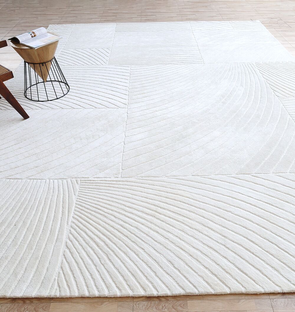 The RAMSHA HOME Viscose & Cotton Handmade Area Rug - HTV 22 (300x400 cm), featuring textured curved and linear patterns in ivory, is displayed on a light wood floor beside a wooden chair and a small metal side table.