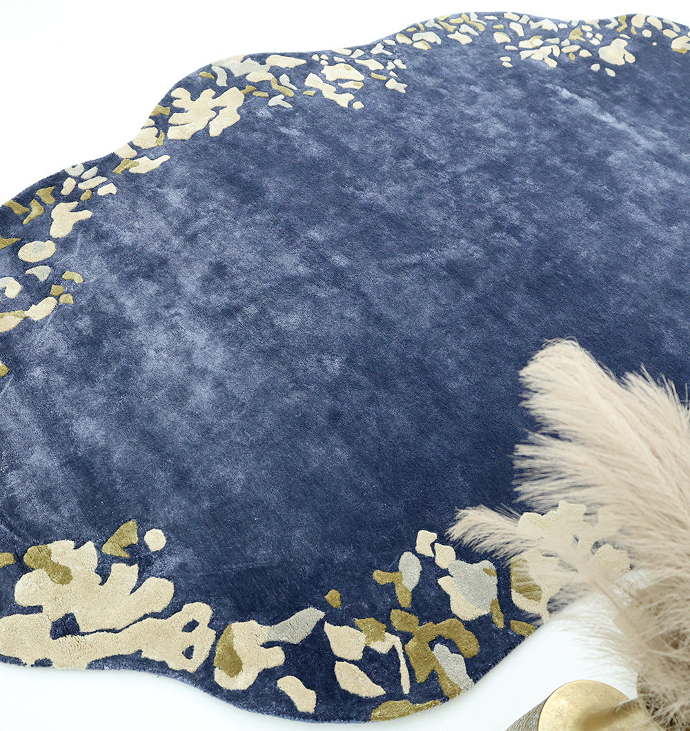 The RAMSHA HOME Navy Blue Viscose Shaped Handmade Carpet 200x300 (HTV-23) showcases gold and cream abstract edge patterns on a navy background, with beige pampas grass partly seen in the lower right corner.