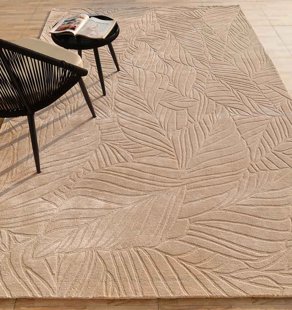 The RAMSHA HOME Rectangle Shape Beige Color Handmade Area Rug - HTV 25 (200x300 cm) sits on a light tiled floor, with part of a black chair and a small round table holding an open magazine placed on the rug.