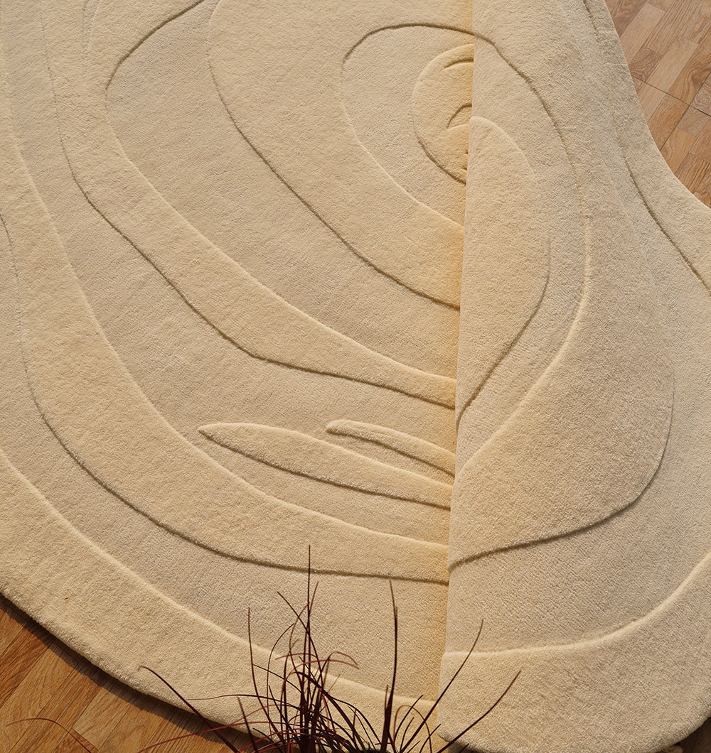 The Natural White Color Handmade Rug - HTW 100 (200X300 cm) by RAMSHA HOME, with raised abstract patterns, lies on a wooden floor. One corner is folded to show its thickness, and some plant stems appear in the foreground.