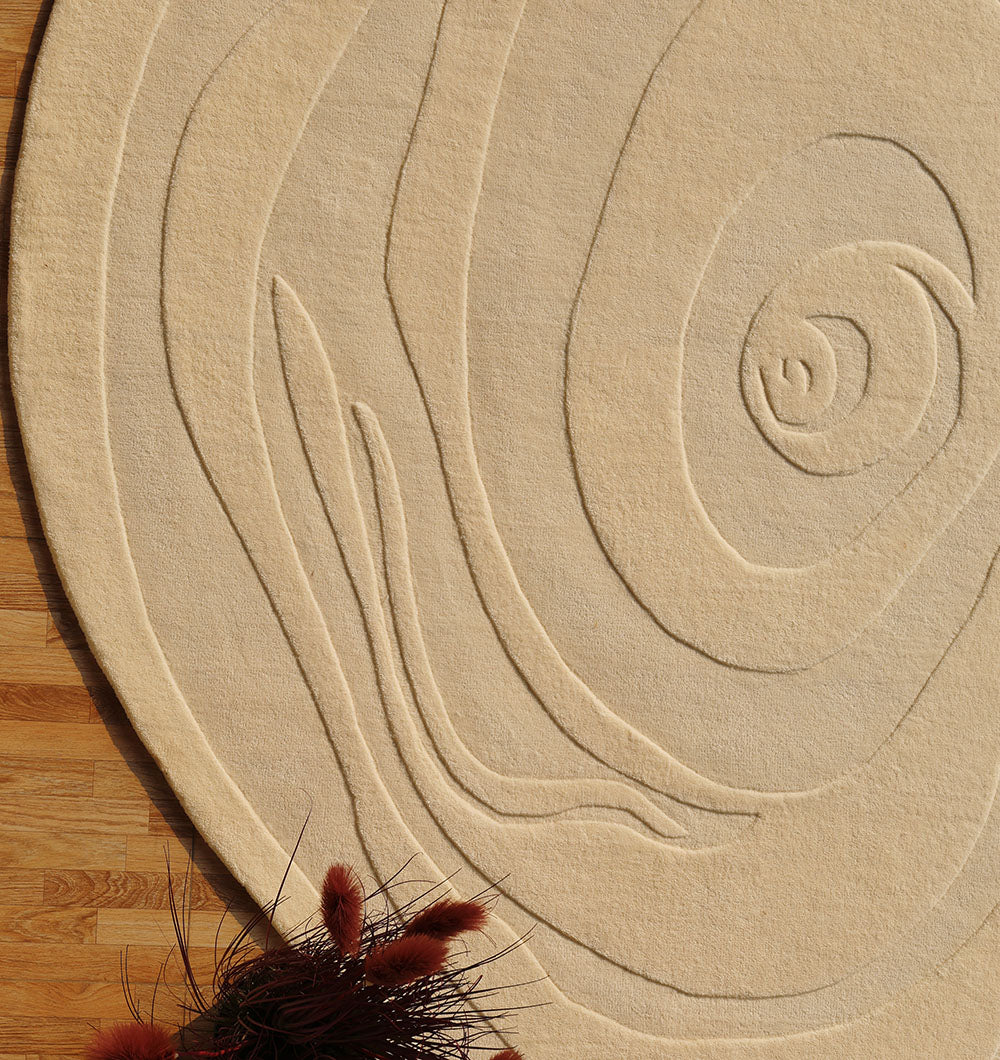 The RAMSHA HOME Natural White Color Handmade Rug - HTW 100 (200x300 cm) lies on a wooden floor, its neutral, textured swirls adding modern style. Hand-tufted in wool, it brings subtle warmth beside a bunch of reddish-brown dried flowers.