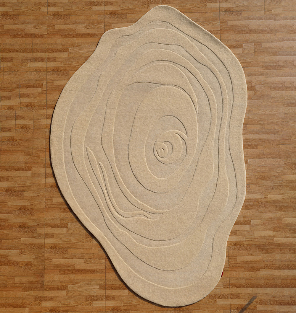 The RAMSHA HOME Natural White Color Handmade Rug - HTW 100 (200x300 cm) features irregular, tree-ring inspired lines and rests on a brown wooden floor, bringing organic charm and modern texture to any contemporary space.